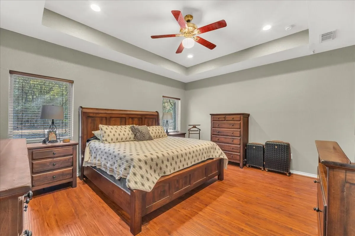Tray ceiling with recessed lighting, ceiling fan, wood-finish flooring, and multiple windows