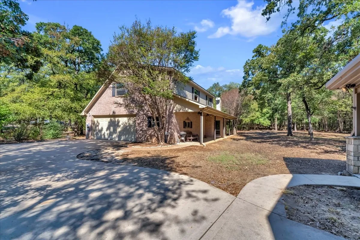 Two-story residence featuring a two-car garage, brick and siding exterior, covered porch, and mature trees