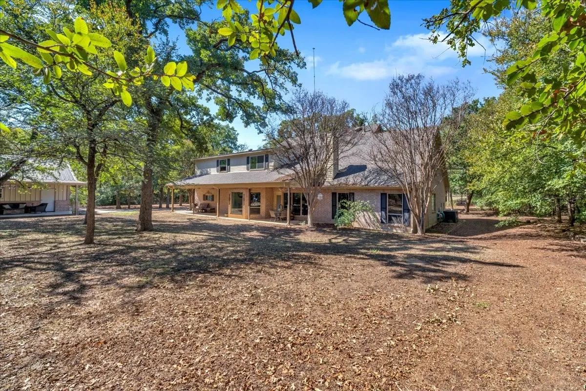 Two covered patios with ceiling fans and stone columns, surrounded by mature trees