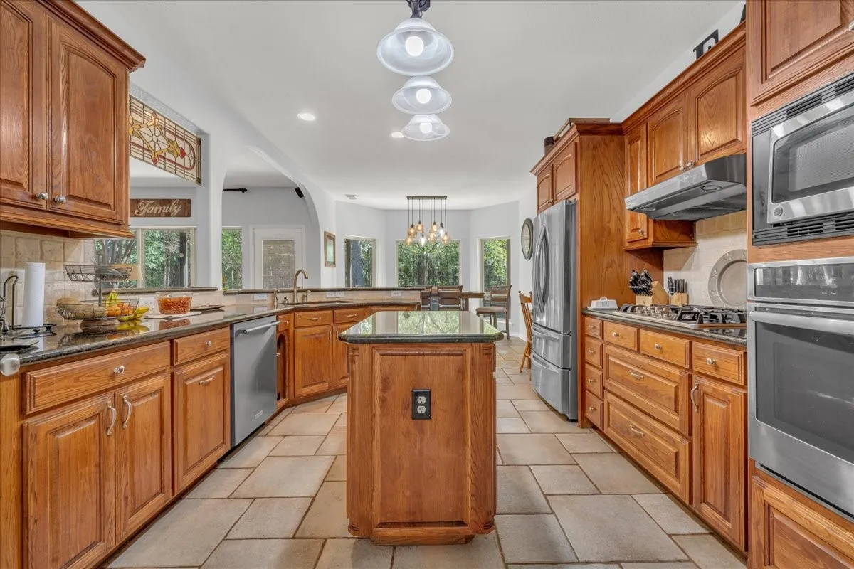 Kitchen featuring wood cabinetry, dark countertops, a center island, stainless steel appliances, and tile flooring