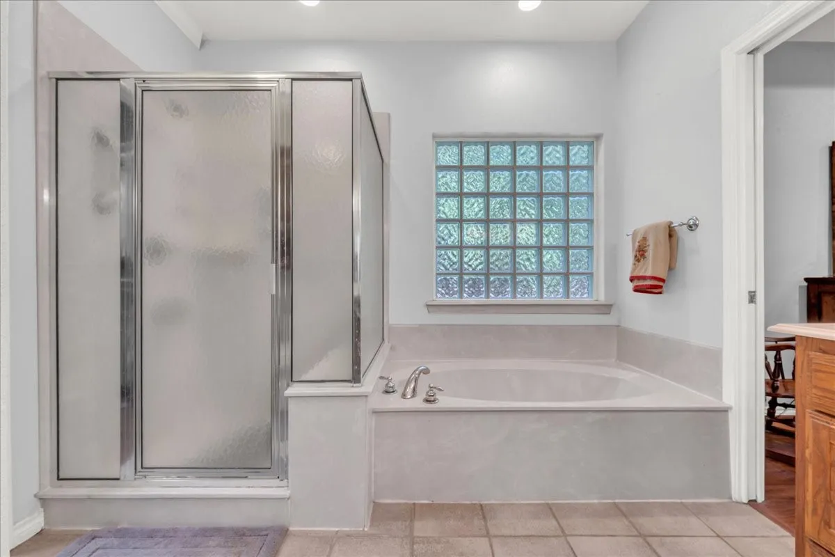 Integrated shower enclosure with frosted glass, built-in soaking tub, glass block window, and recessed lighting