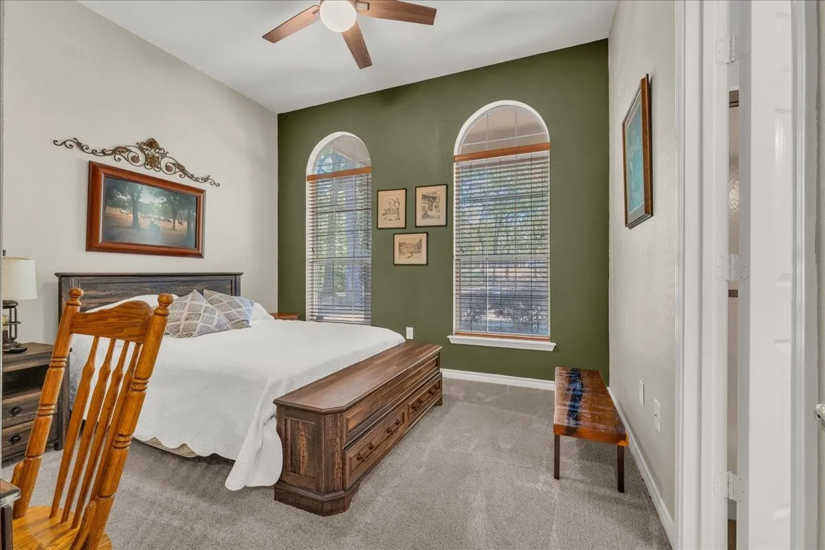 Vaulted ceiling with a ceiling fan, two arched windows with blinds, and carpeted flooring