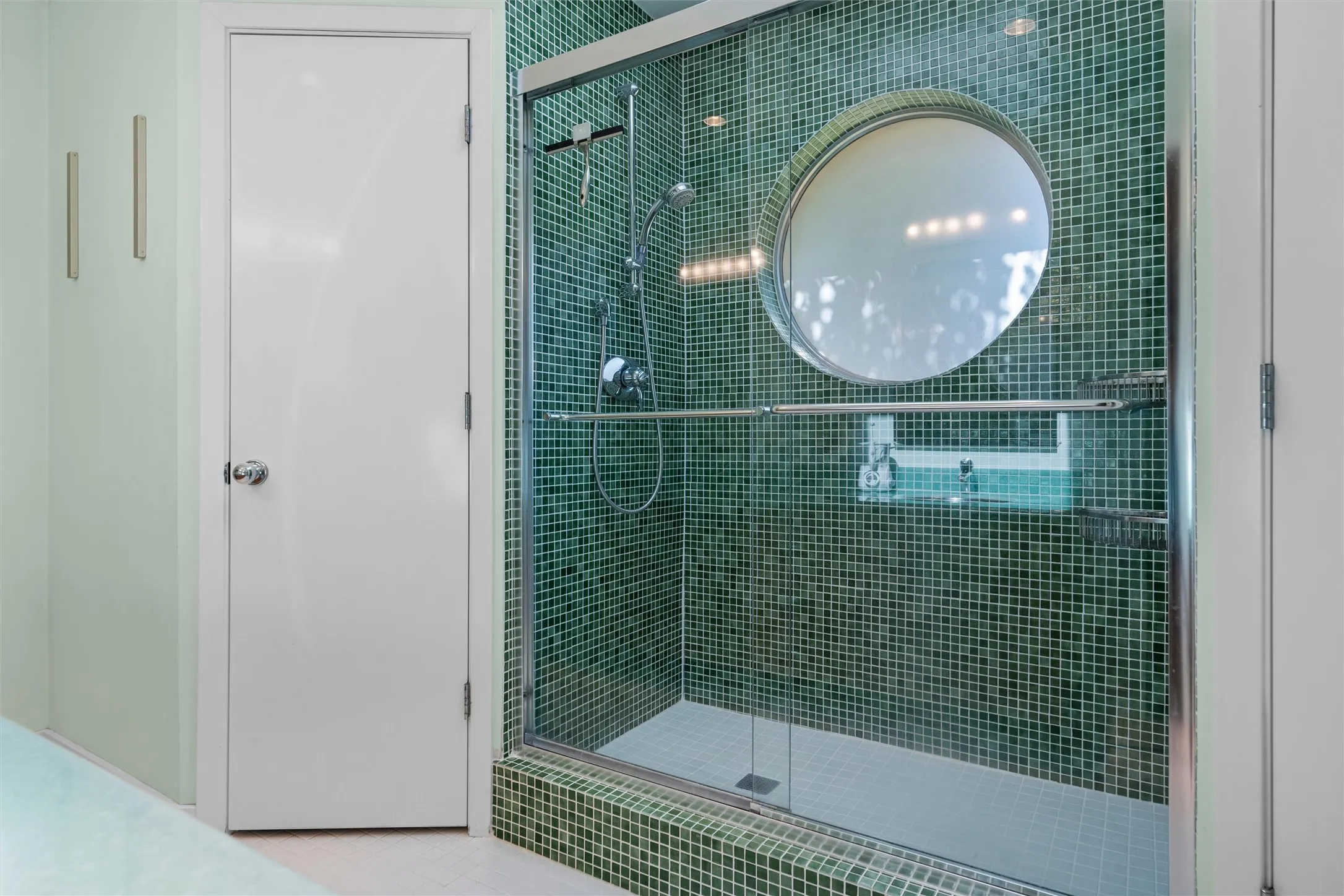 Custom designed glass tiled walk in shower with glass door.