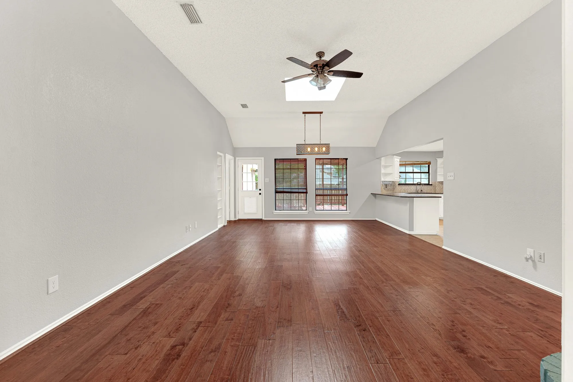 A dramatic vaulted ceiling stretches across warm wood-tone flooring, creating a vast sense of openness highlighted by natural overhead light. Picture gathering everyone together for a lively movie marathon as soft evening light glows through the back windows