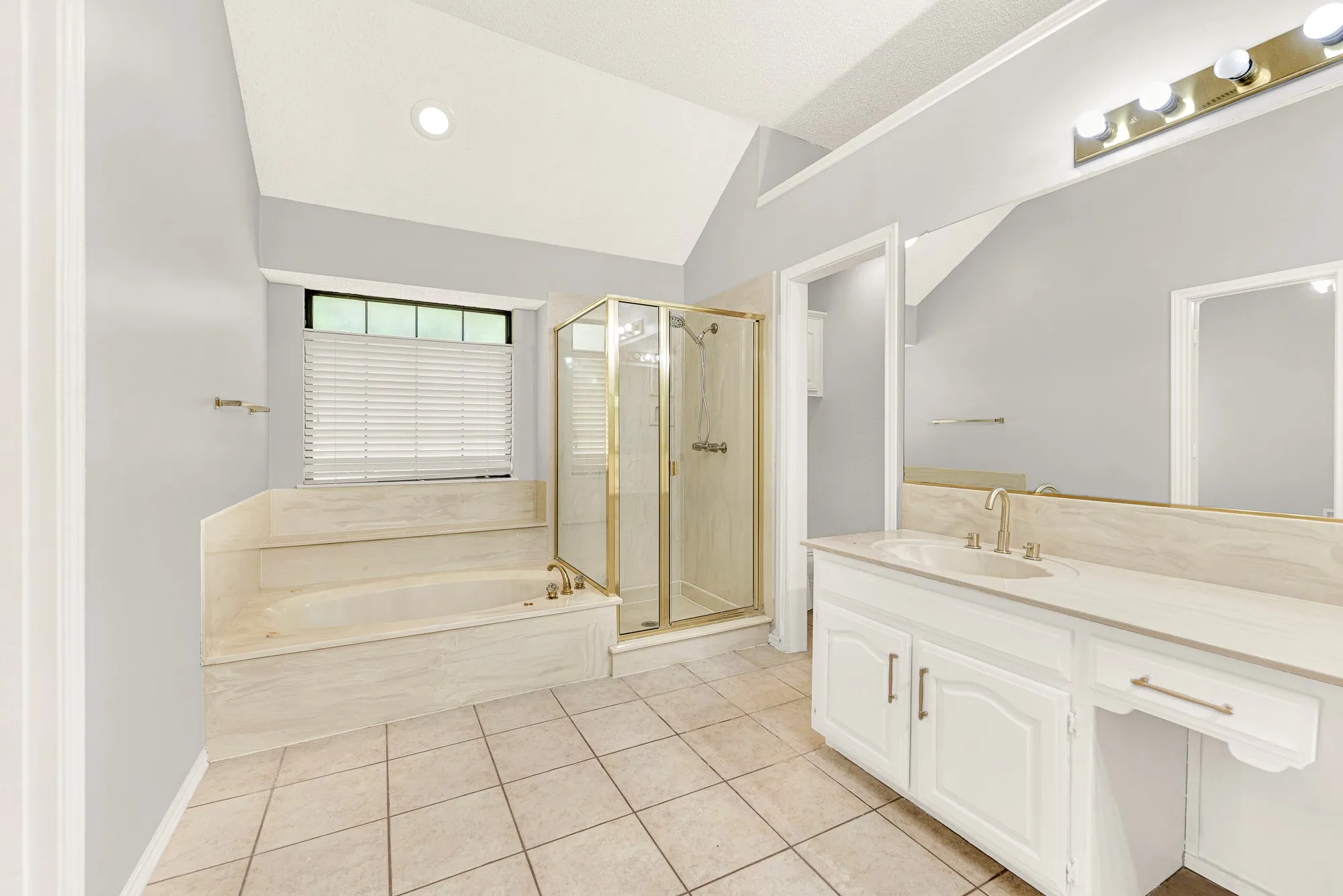 A deep soaking tub sits tucked under a bright window, surrounded by neutral tile and a separate glass shower. Unwind here after a busy week with a hot bubble bath and soothing candlelight.