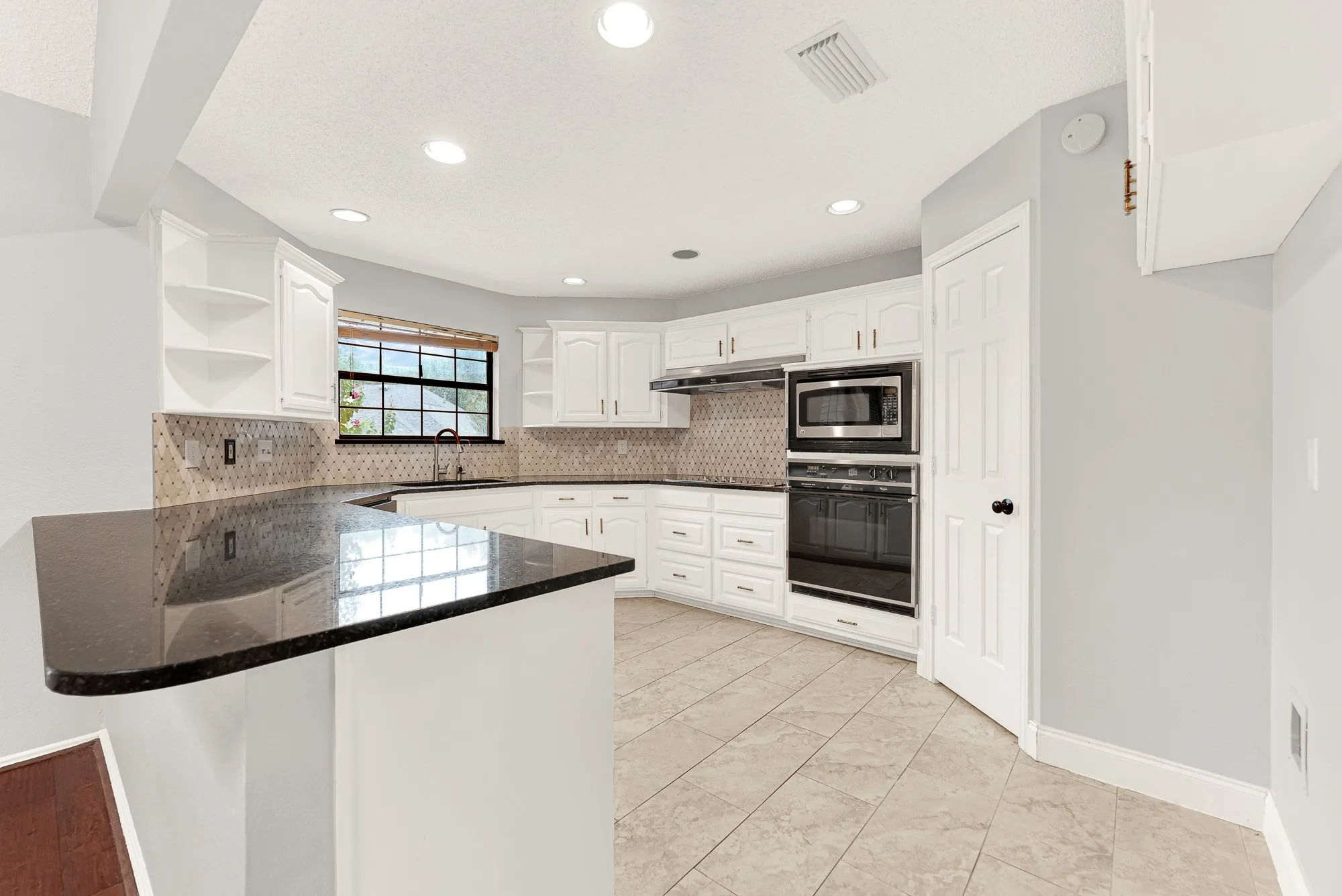Deep polished granite countertops sweep around bright cabinetry, reflecting crisp recessed ceiling lighting throughout the culinary space. You will love pouring morning juice here while checking emails in this open, functional kitchen