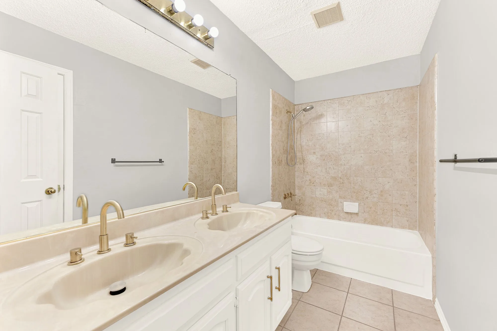 Warm neutral tilework wraps around a built-in tub and shower, complemented by a wide double-sink vanity. You can easily envision your guests enjoying a refreshing, hotel-like morning routine in complete comfort.