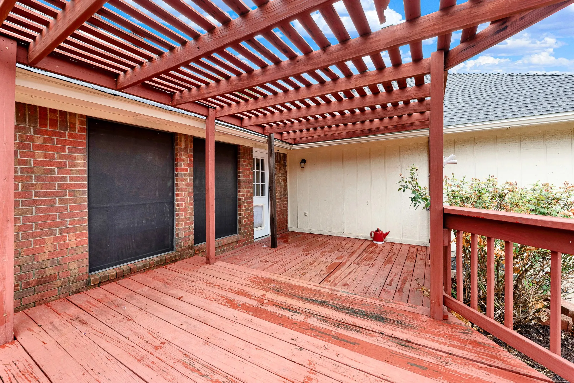Warm red brick meets extended decking underneath slatted beams, connecting interior doorways directly to outdoor living. Imagine firing up the grill for weekend barbecues while music plays softly under the pergola canopy