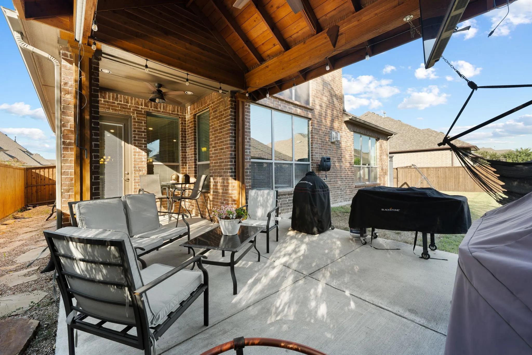 Expansive covered patio with wood beam ceiling and integrated shade structure, featuring a concrete floor and large sliding glass doors opening to the residence
