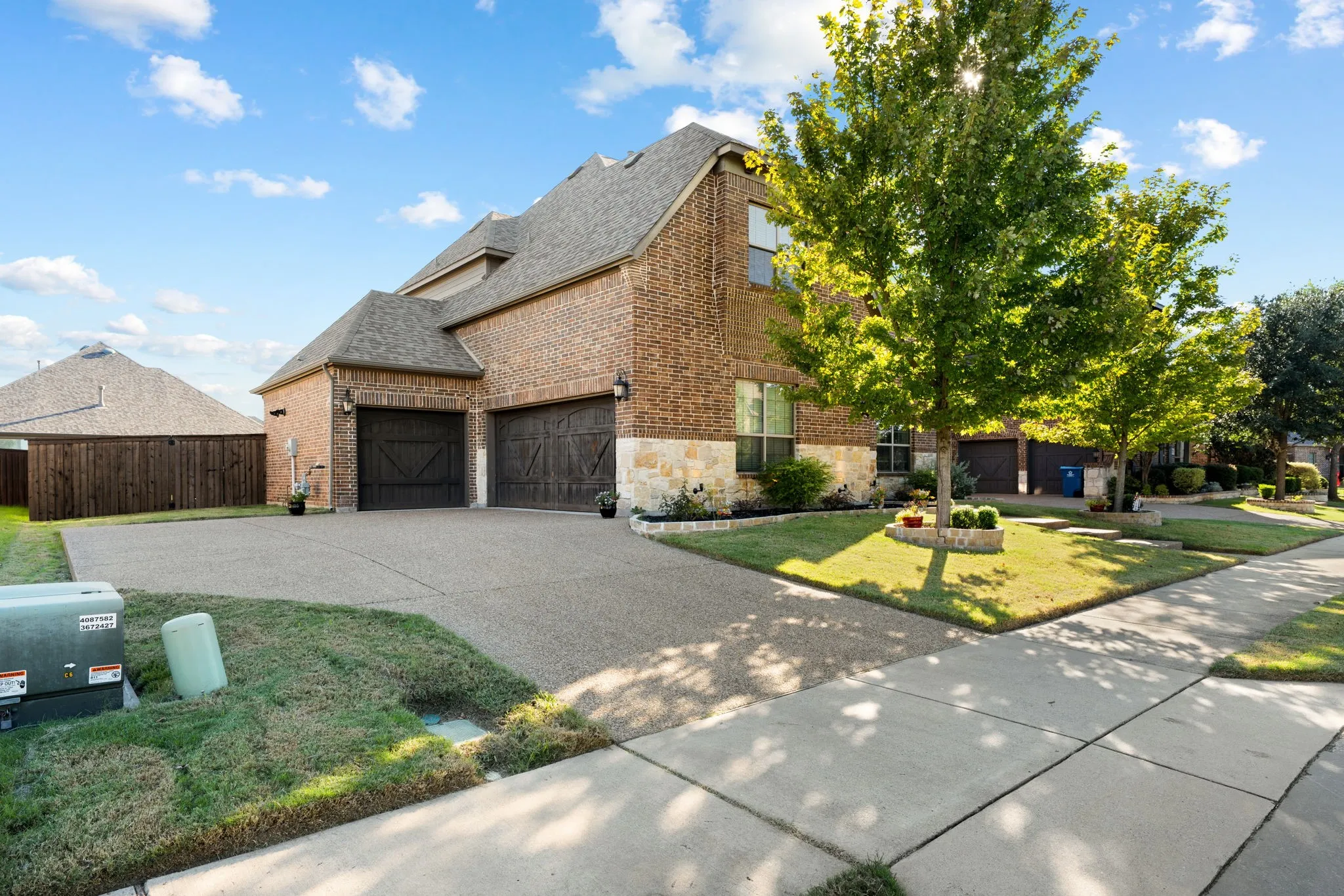 Brick and stone facade with a multi-car driveway, two dark wood-finish garage doors, and a manicured front lawn