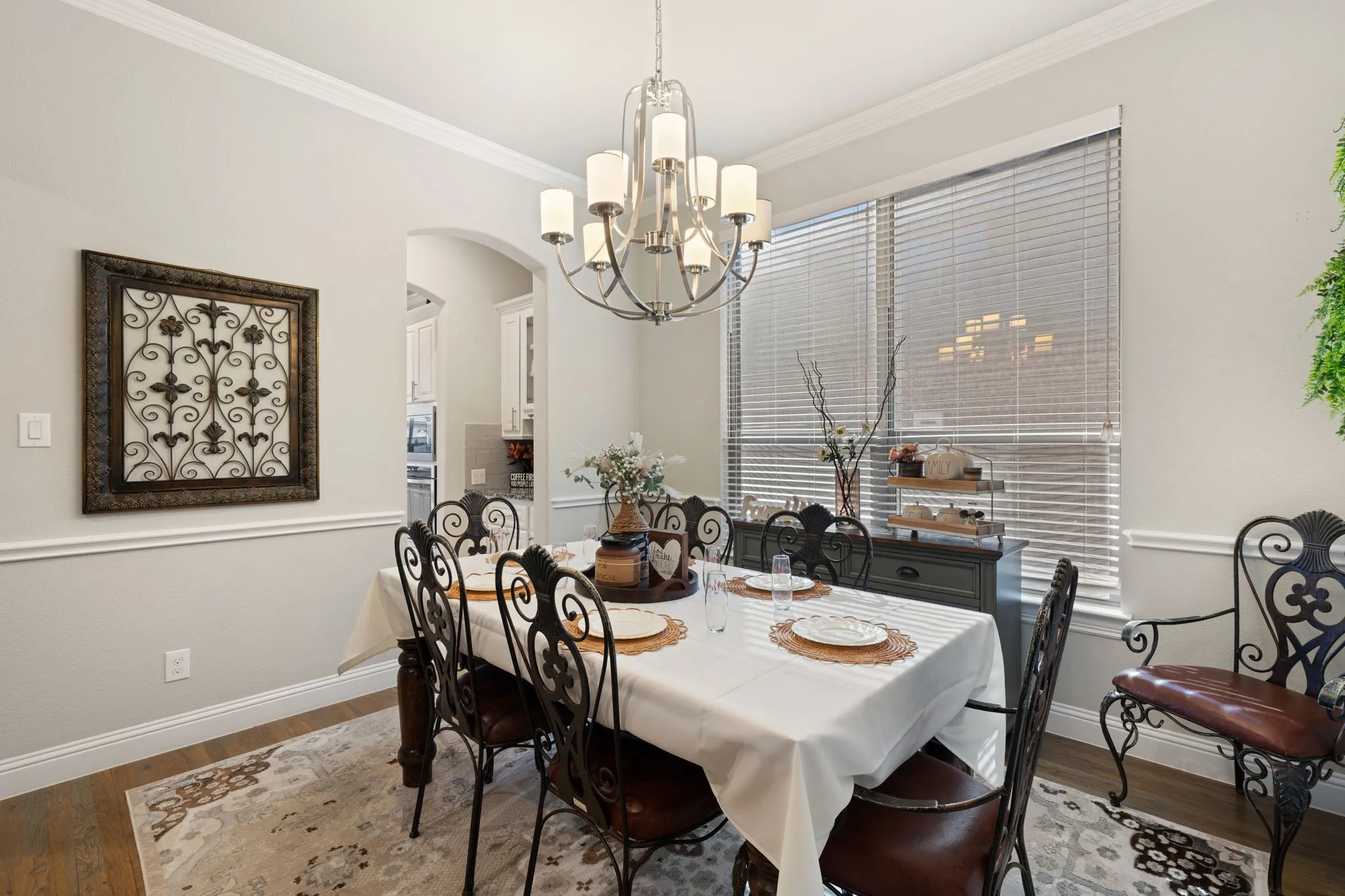 Wood-finish flooring, crown molding, chair rail molding, arched doorway, and chandelier lighting
