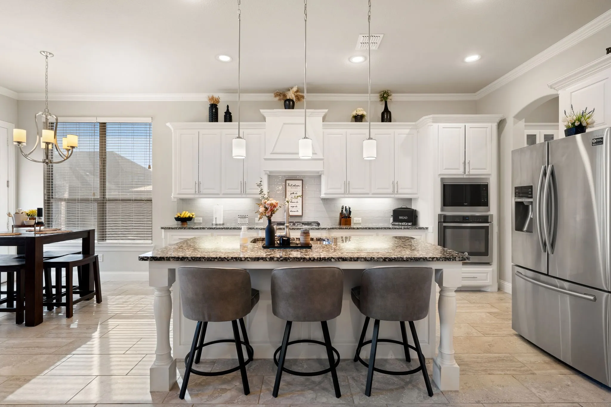 Spacious kitchen featuring an expansive center island with seating, white cabinetry, built-in stainless steel appliances, and tiled flooring