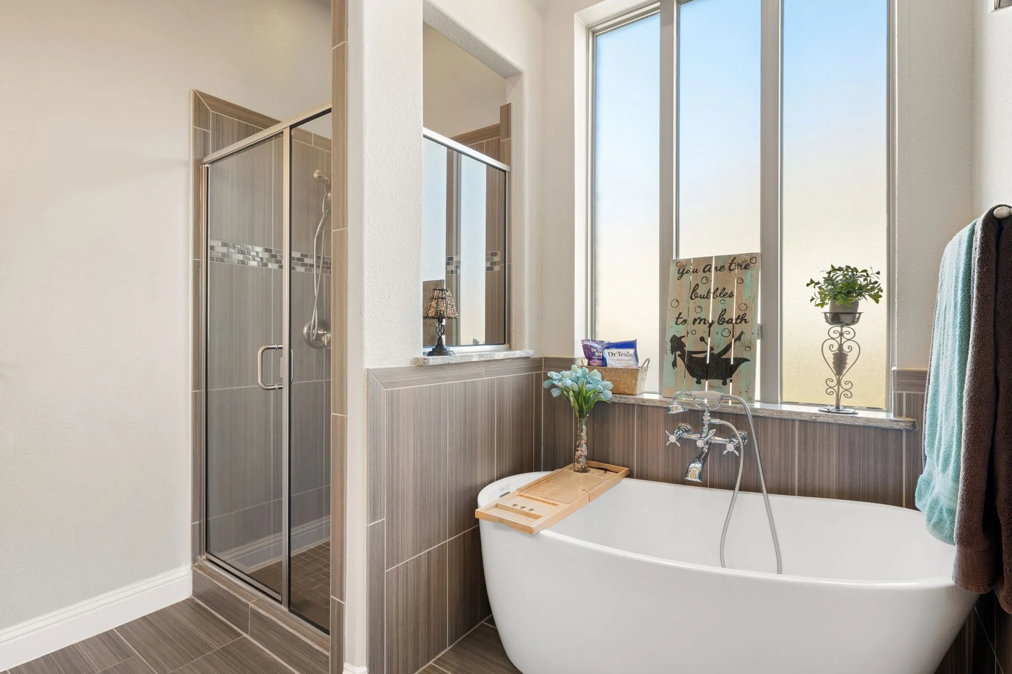 Freestanding soaking tub with chrome fixtures, glass-enclosed shower with tile surround, large window, and wood-finish wall paneling