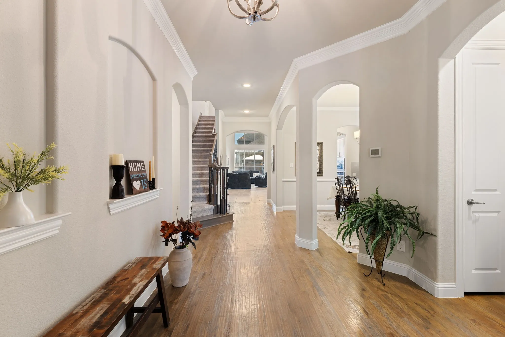 Expansive hallway with wood-finish flooring, arched doorways, crown molding, and a staircase with carpeted treads and dark wood banister