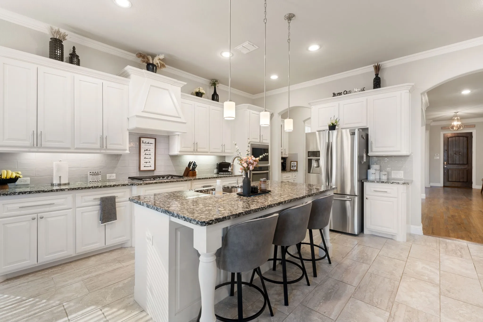 White cabinetry with crown molding, stone countertops, stainless steel appliances, tile flooring, and a central island with pendant lighting