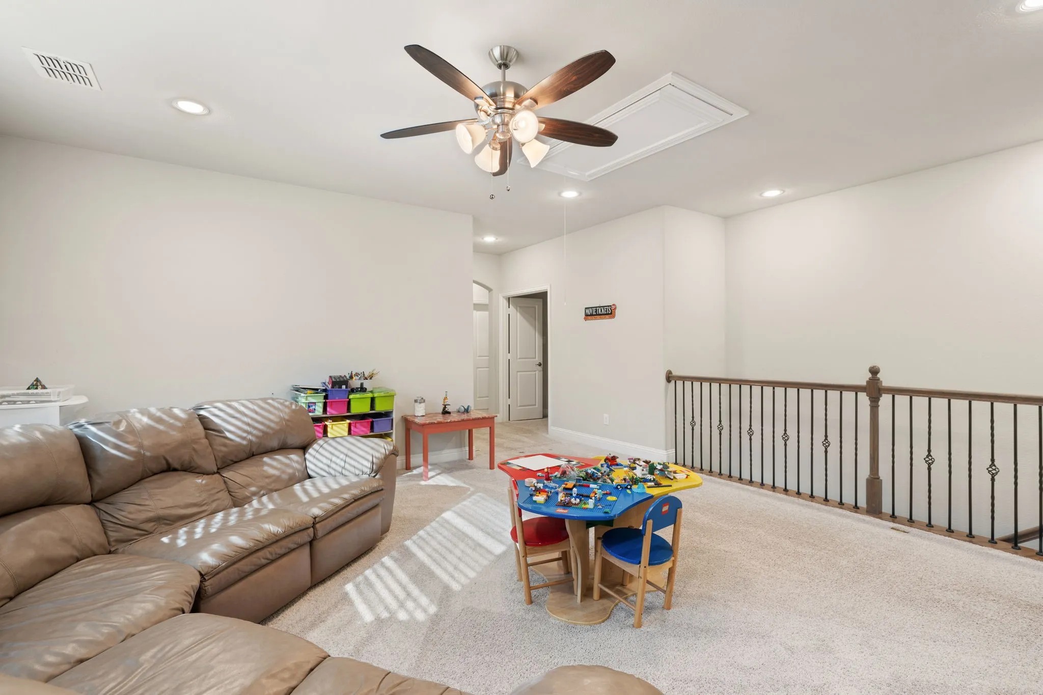 Carpeted loft area featuring a ceiling fan with integrated lighting, recessed lighting, and a wrought iron and wood baluster railing
