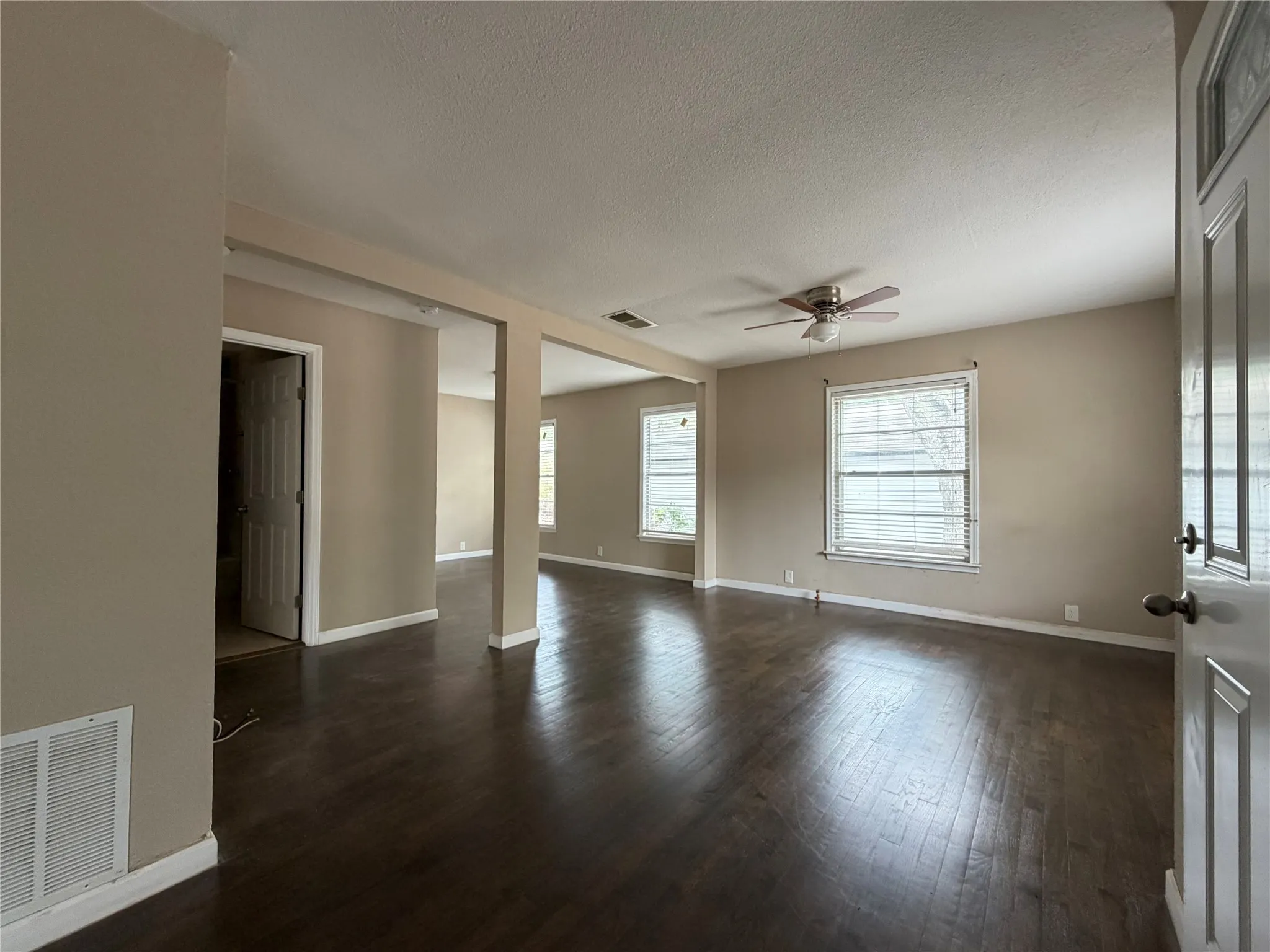 Spacious interior with wood-finish flooring, neutral wall tones, multiple windows with blinds, and a ceiling fan with integrated lighting