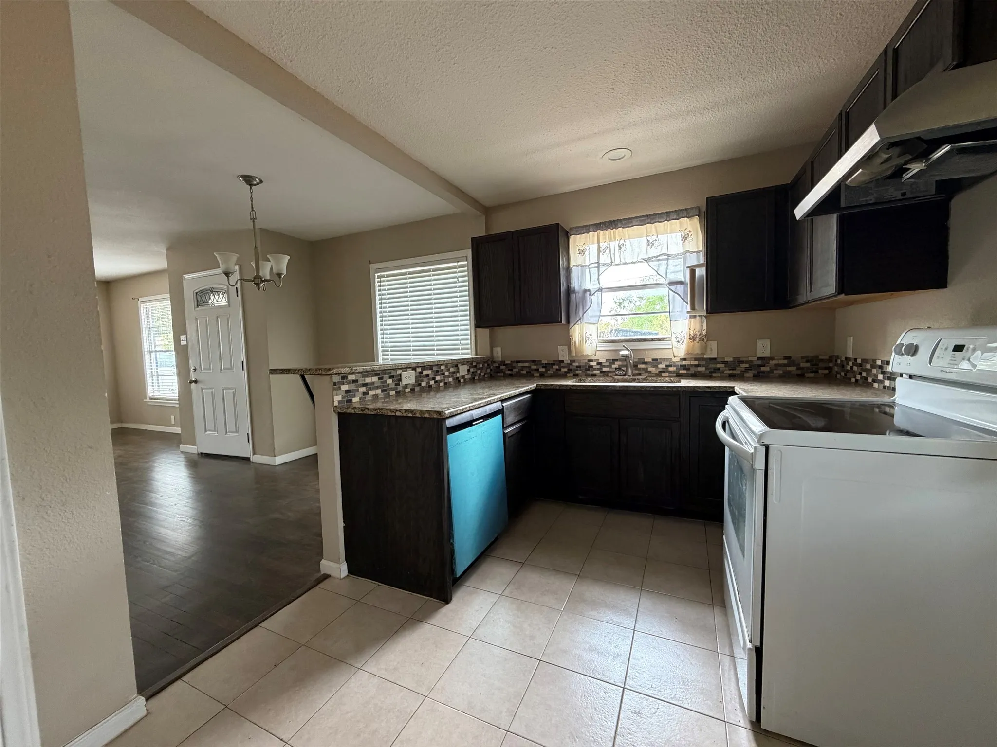 Kitchen featuring dark wood-finish cabinetry, tile flooring, stone countertops, and a mosaic tile backsplash