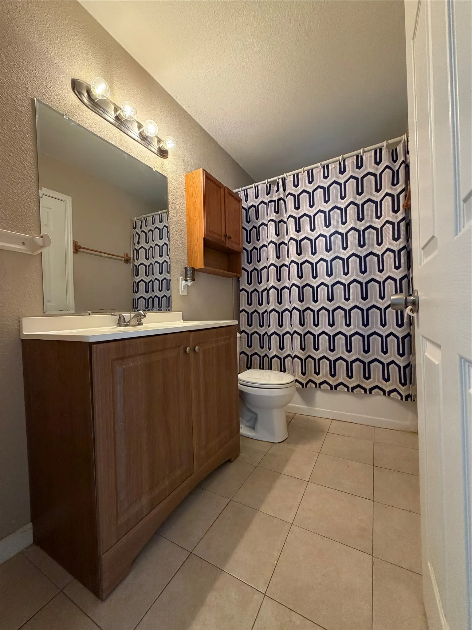 Bathroom featuring a wood-finish vanity with an integrated sink, a large wall-mounted mirror, and tile flooring