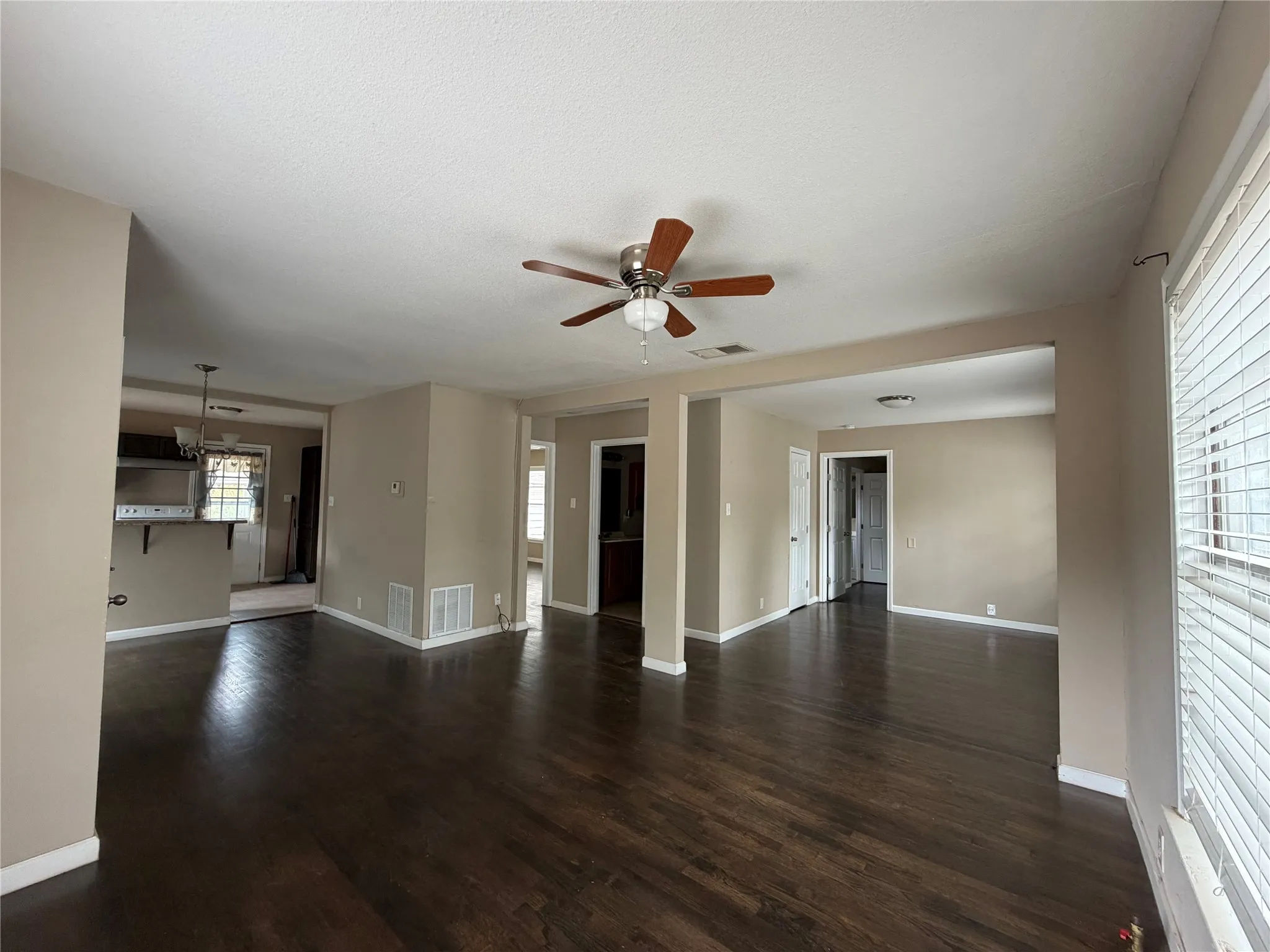 Expansive room featuring wood-finish flooring, a ceiling fan with integrated lighting, and multiple windows with blinds