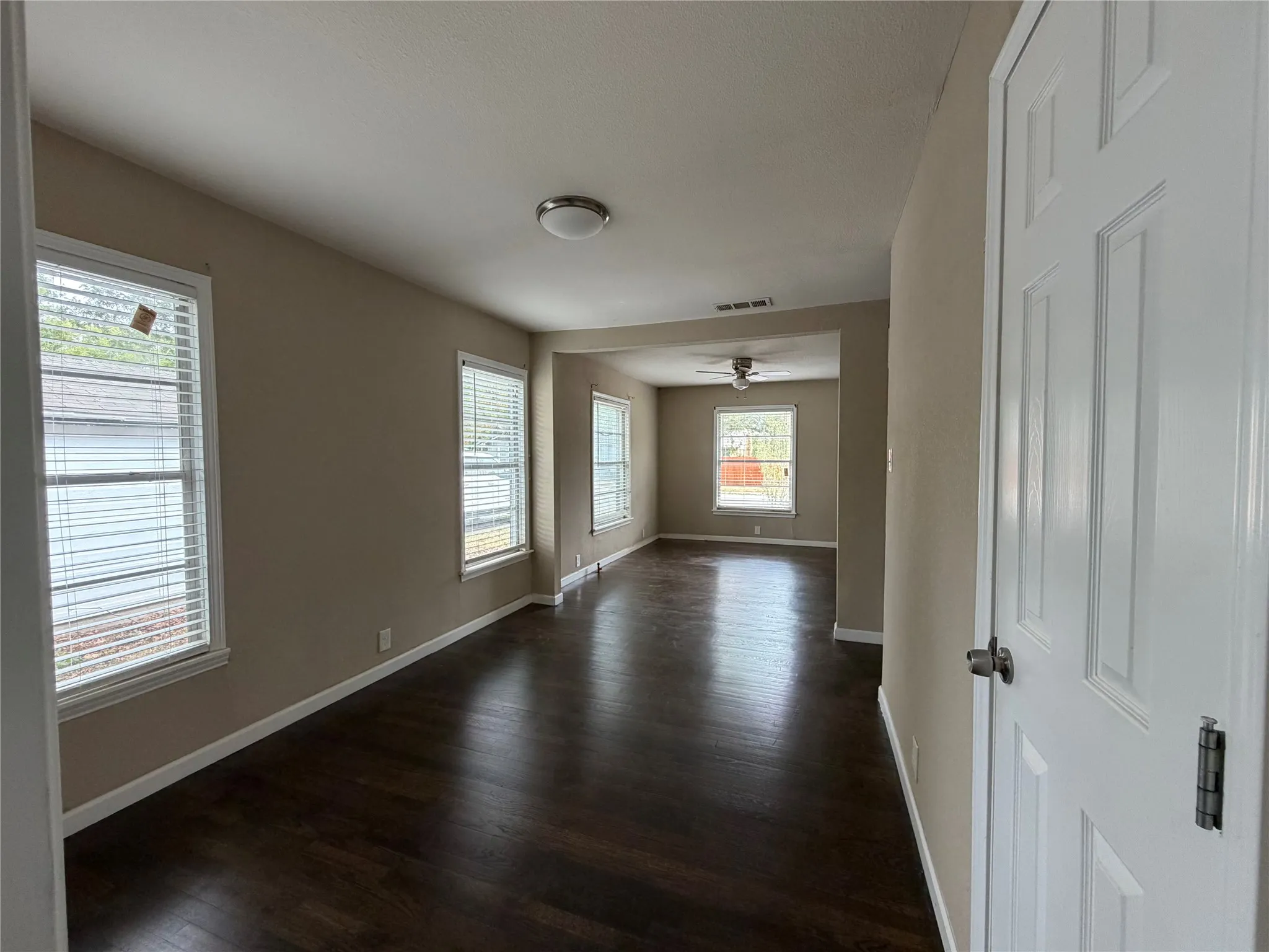 Dark wood-finish flooring throughout, multiple windows with blinds, and a neutral wall color