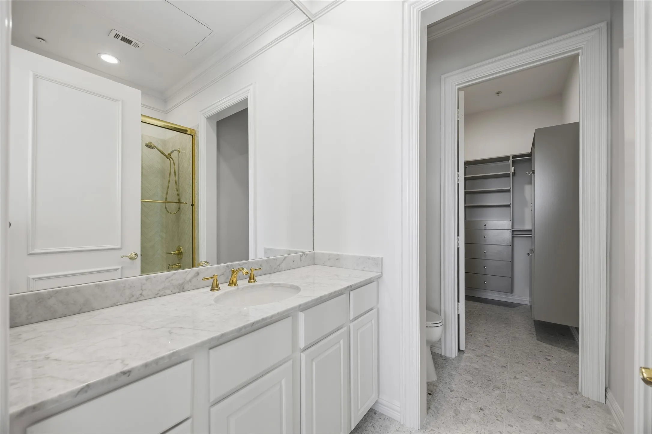 White vanity with a stone countertop and gold-finish fixtures