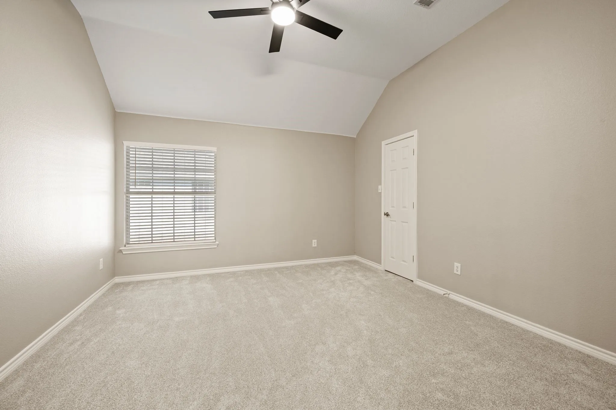 A comfortable secondary bedroom features a vaulted ceiling, neutral colors & a ceiling fan, ready for your personal touch.