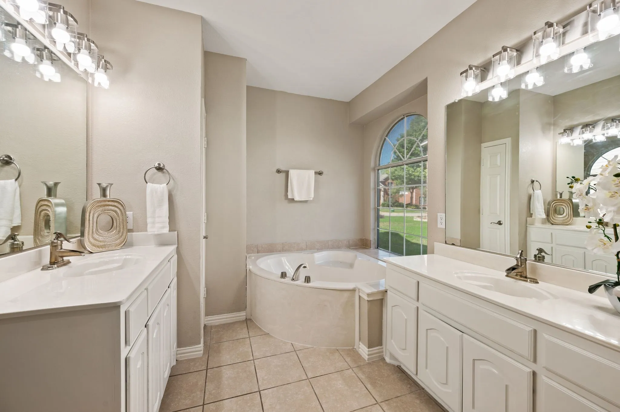 Two spacious vanities offer room to spread out, while an arched window brings beautiful natural light to the soaking tub.