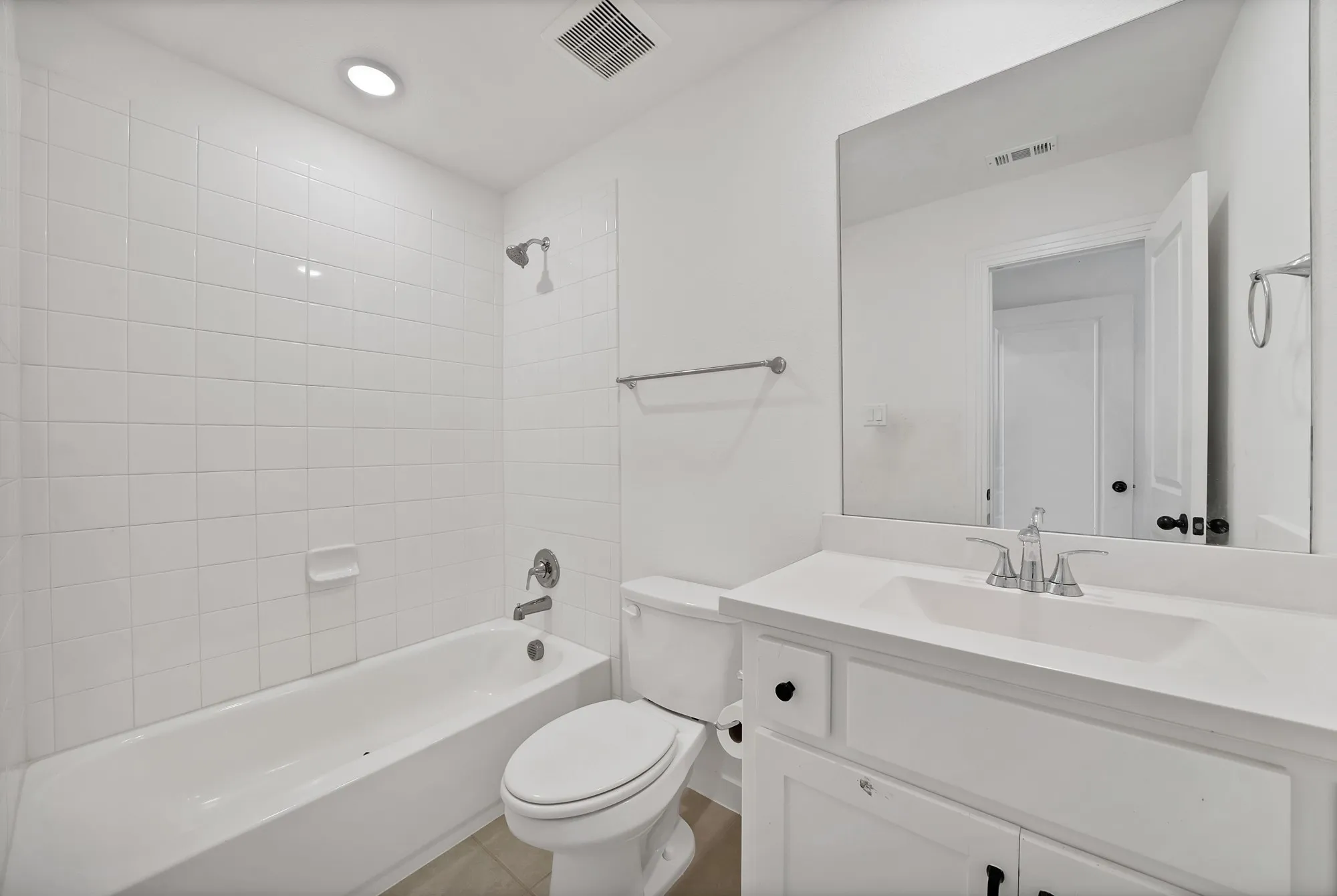 White tile bath surround, recessed lighting, chrome shower fixture, vanity with integrated sink, and large wall mirror