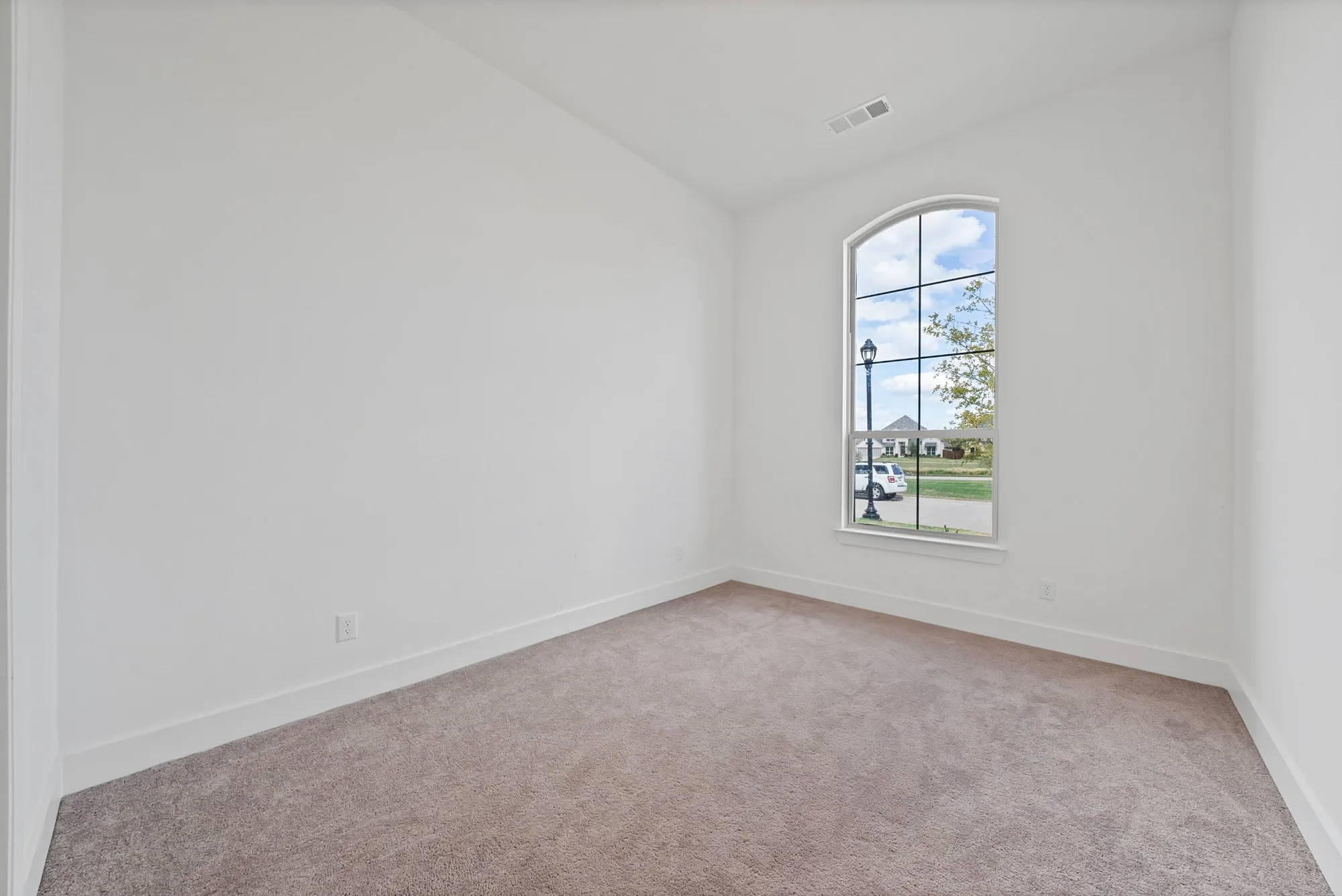 Arched window with gridded panes, light neutral carpeting, and white walls