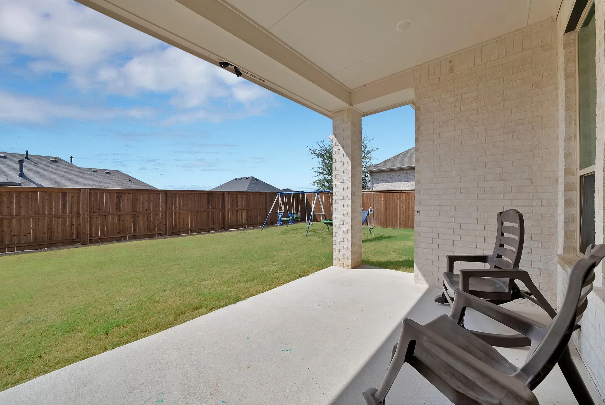 Covered patio with a concrete surface, white brick exterior, and a spacious green lawn
