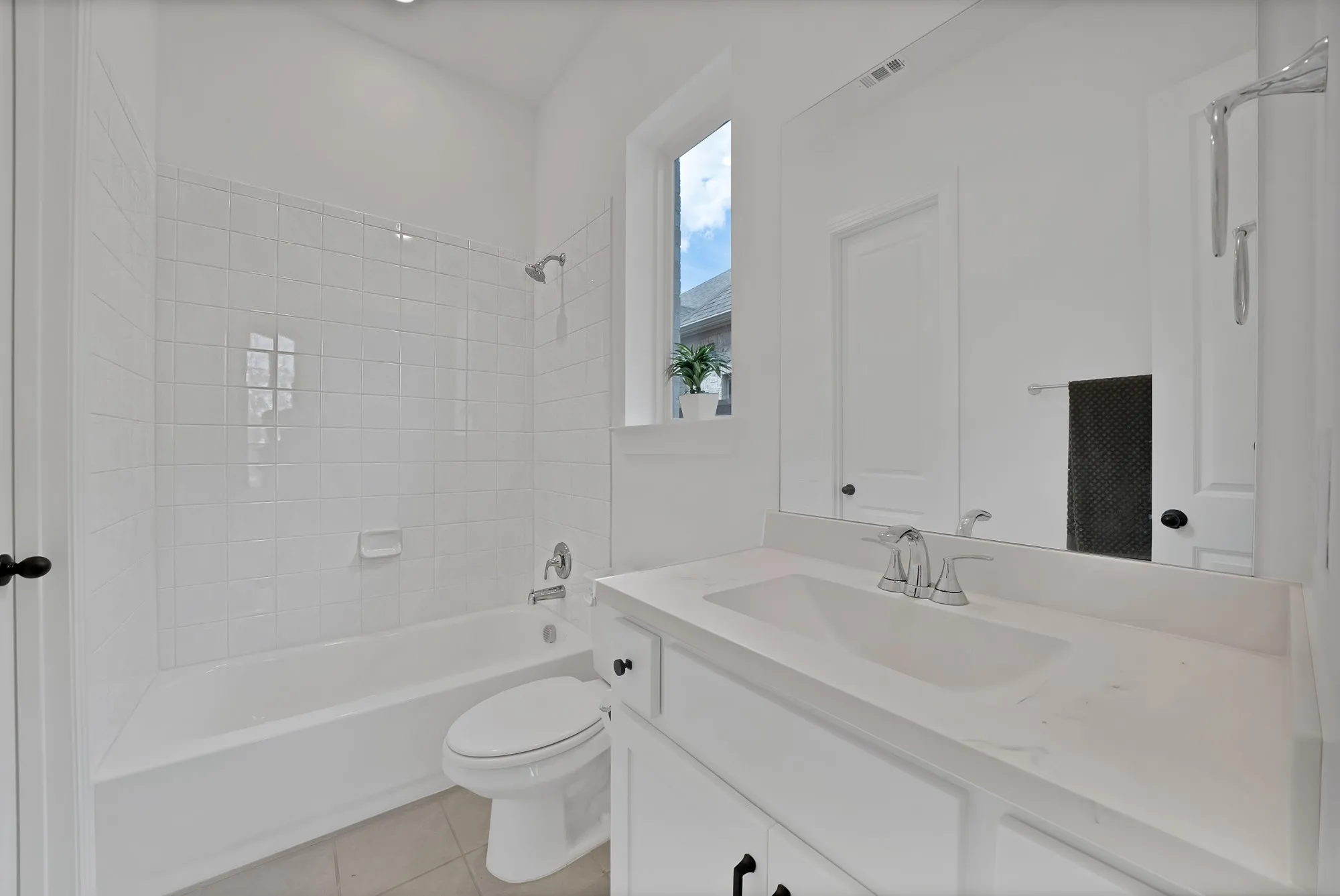 White tile tub/shower combination, single vanity with integrated sink, polished chrome fixtures, and neutral floor tiling
