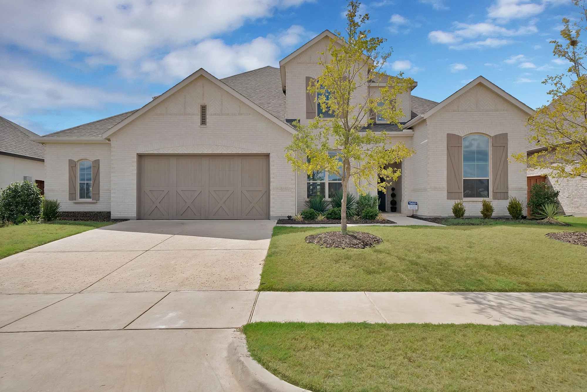 Light brick exterior with contrasting roof, front-facing two-car garage, concrete driveway, and front lawn
