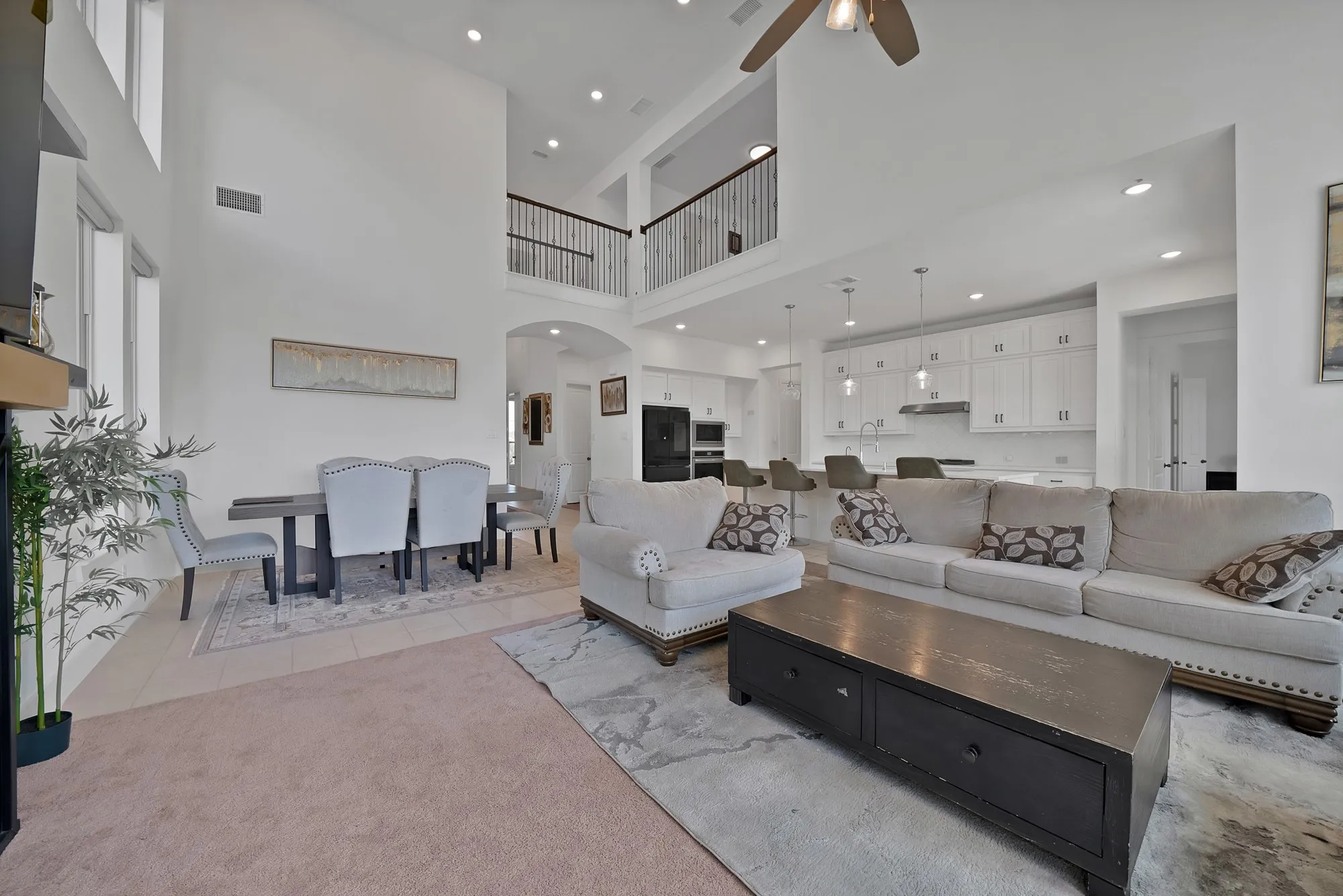 Open-concept living space featuring high ceilings, a second-story balcony, recessed lighting, and a kitchen with white cabinetry and pendant lighting