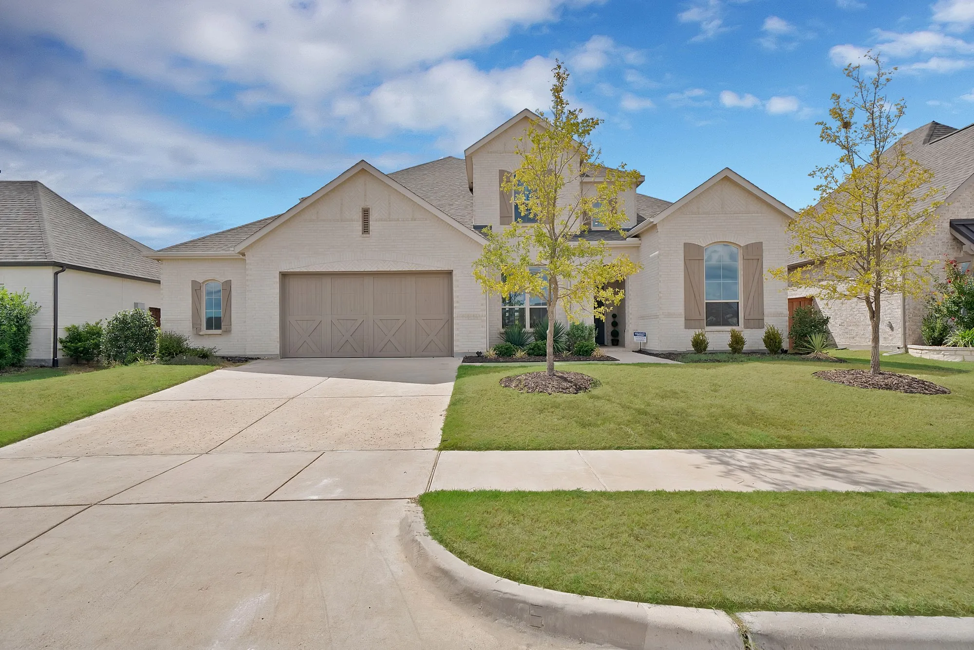 Light-colored brick and stucco exterior with a two-car garage, established front landscaping, and a concrete driveway