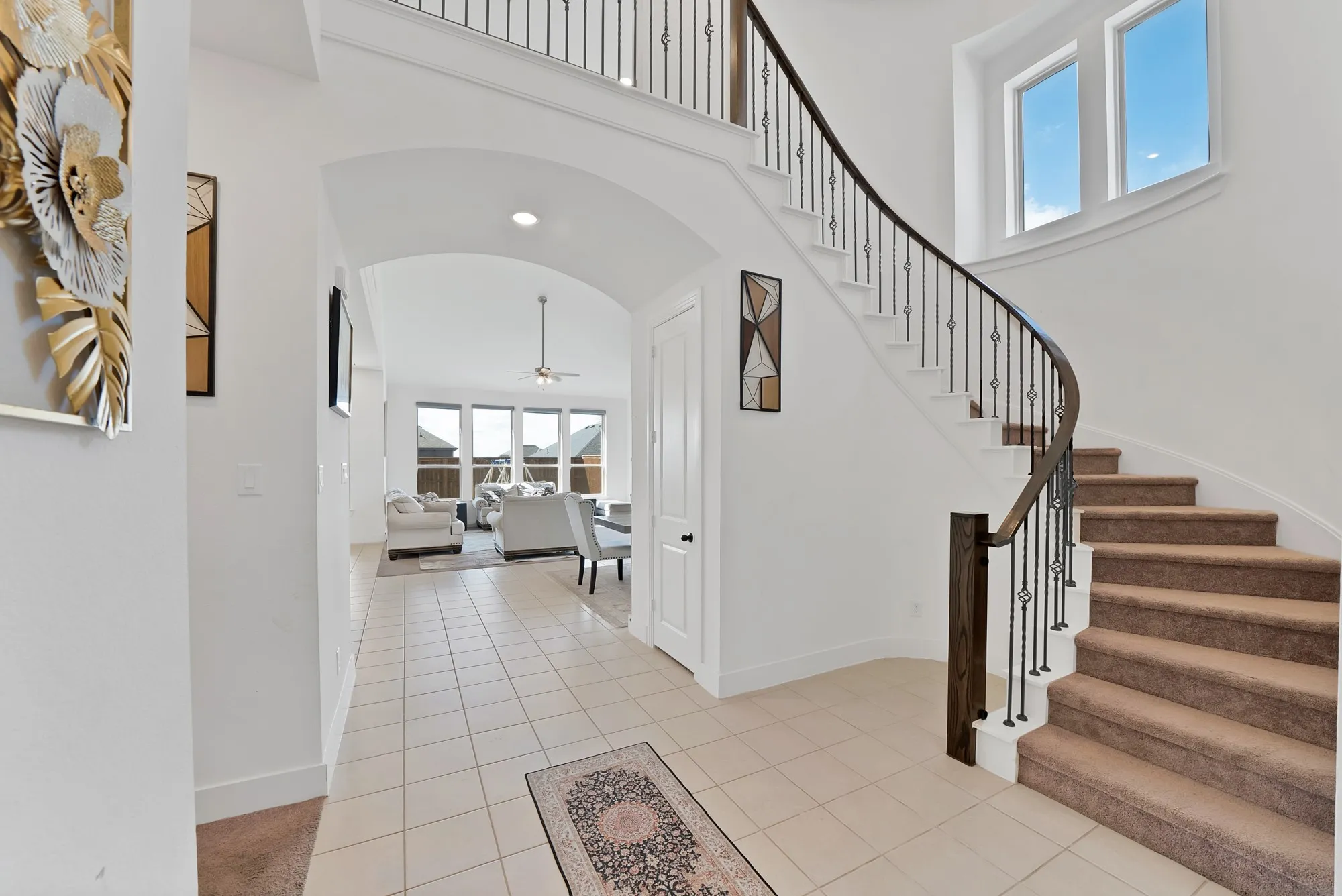 Curved staircase with metal balusters, tile flooring, arched entryway, and upper-level windows