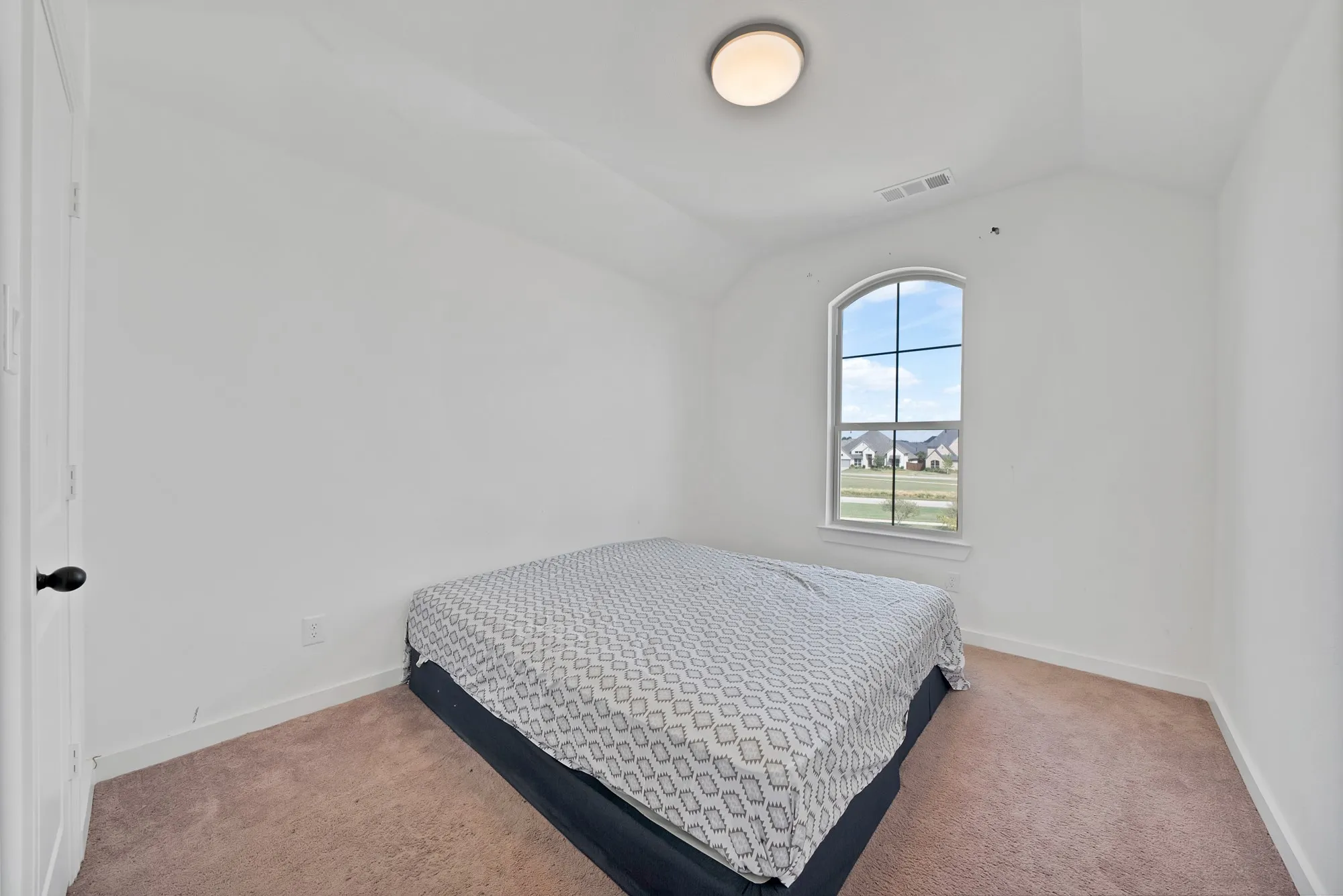 Arched window with exterior setting, vaulted ceiling, flush mount ceiling light, and neutral carpet flooring