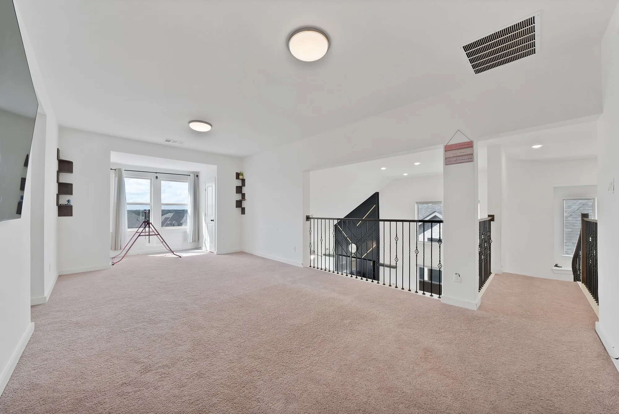 Spacious carpeted room featuring a large window, recessed lighting, and an open railing overlooking the floor below