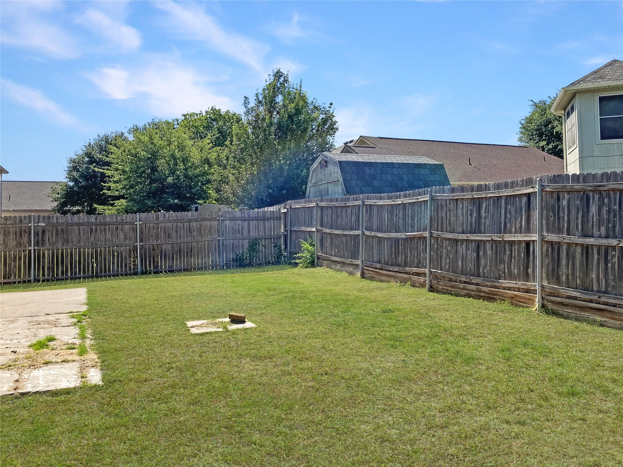 Expansive backyard featuring a wood fence and a concrete patio section