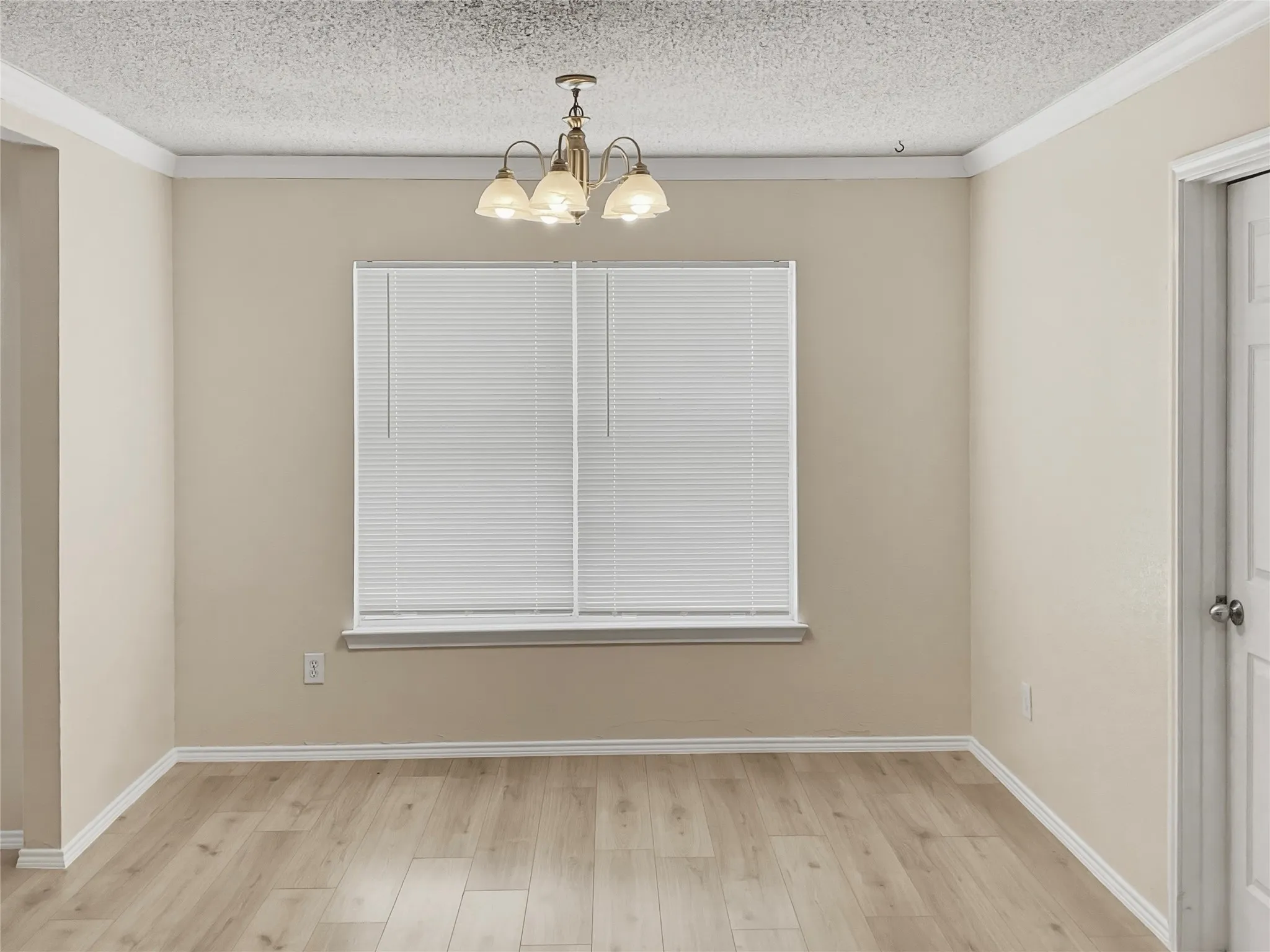Wood-finish flooring, crown molding, white window blinds, and a brass-tone chandelier with frosted glass shades