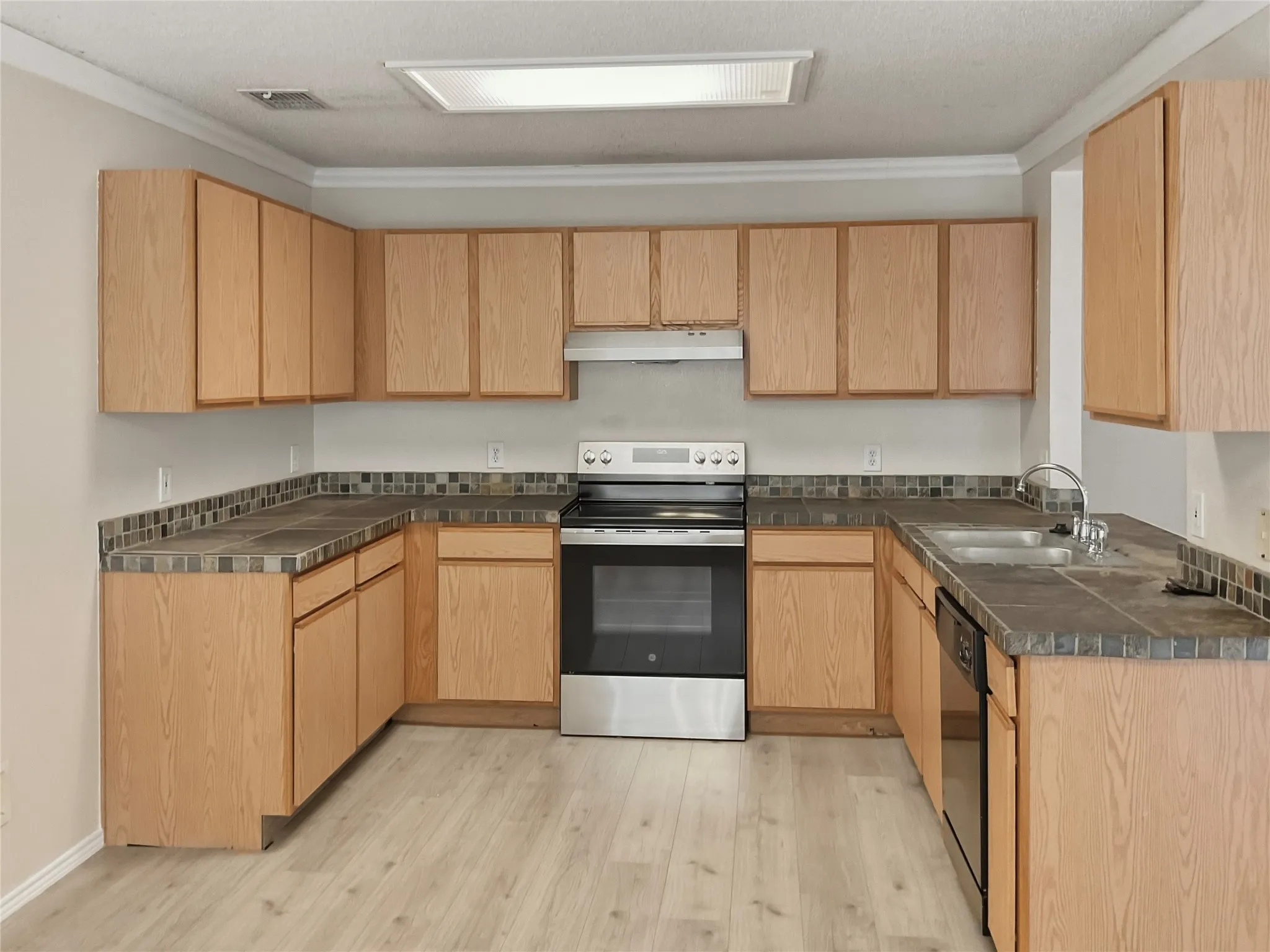U-shaped kitchen layout featuring wood-finish cabinetry, tile countertops, and a tile backsplash