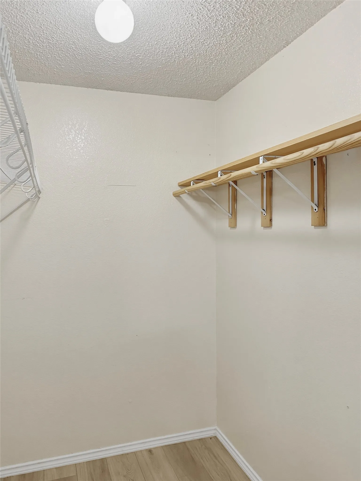 Spacious walk-in closet featuring natural wood-finish shelving and hanging rod system, recessed ceiling lighting, and wood-finish flooring throughout