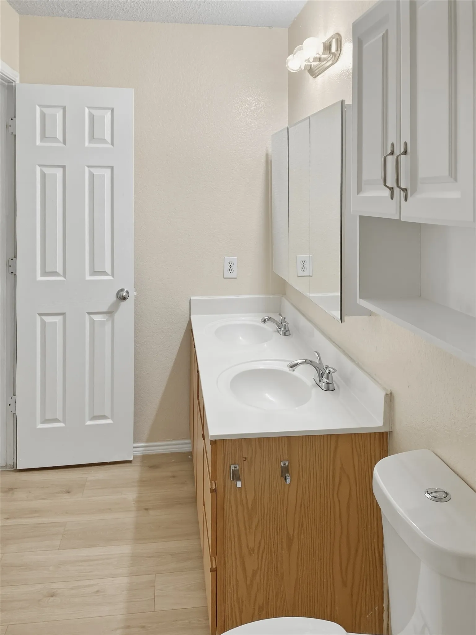 Dual vanity with integrated sinks, wood-finish cabinetry, white countertops, and wood-finish flooring