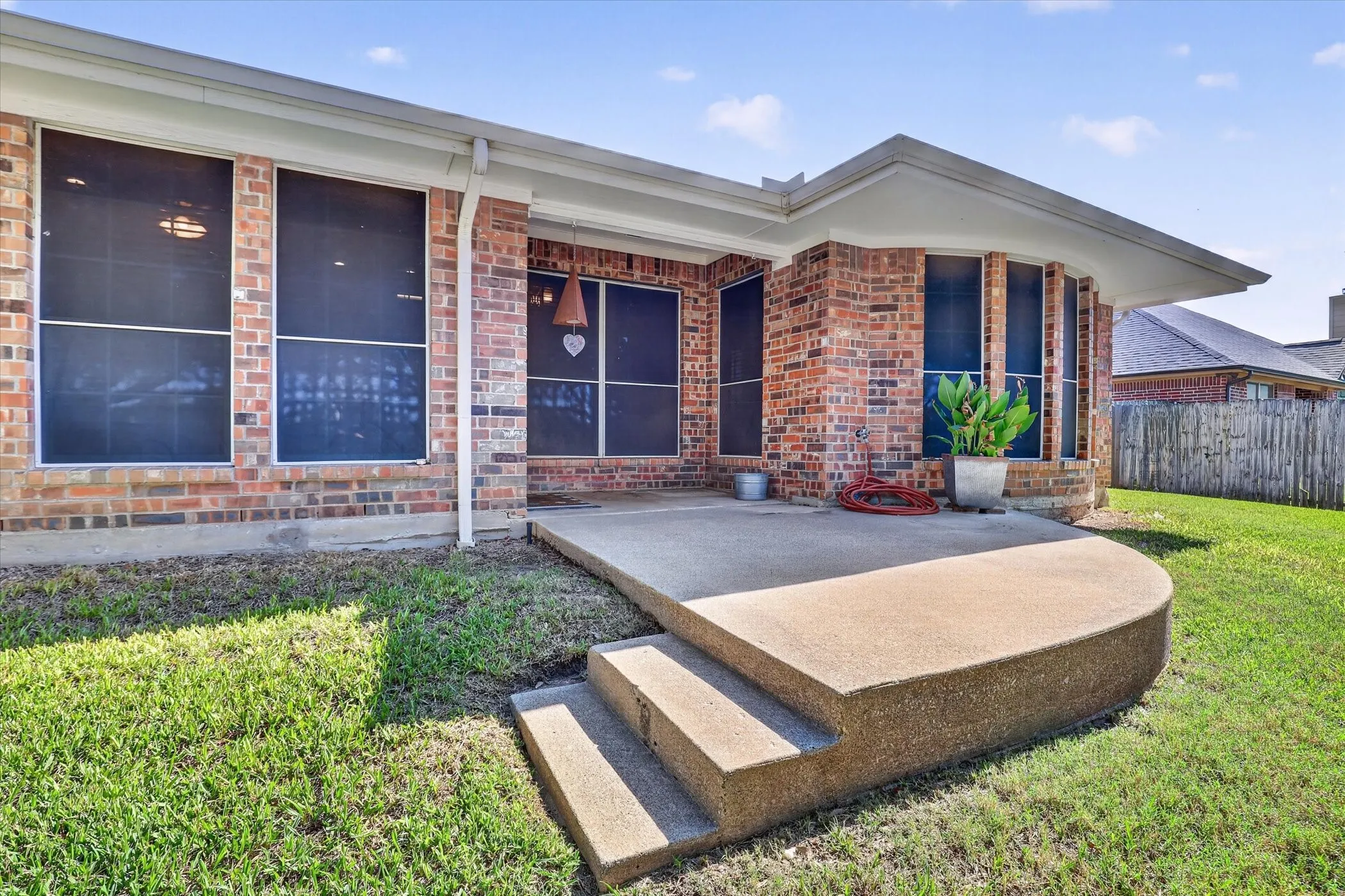 Brick home featuring expansive front porch with concrete stepped entry, large multi-pane windows, and manicured lawn with mature landscaping