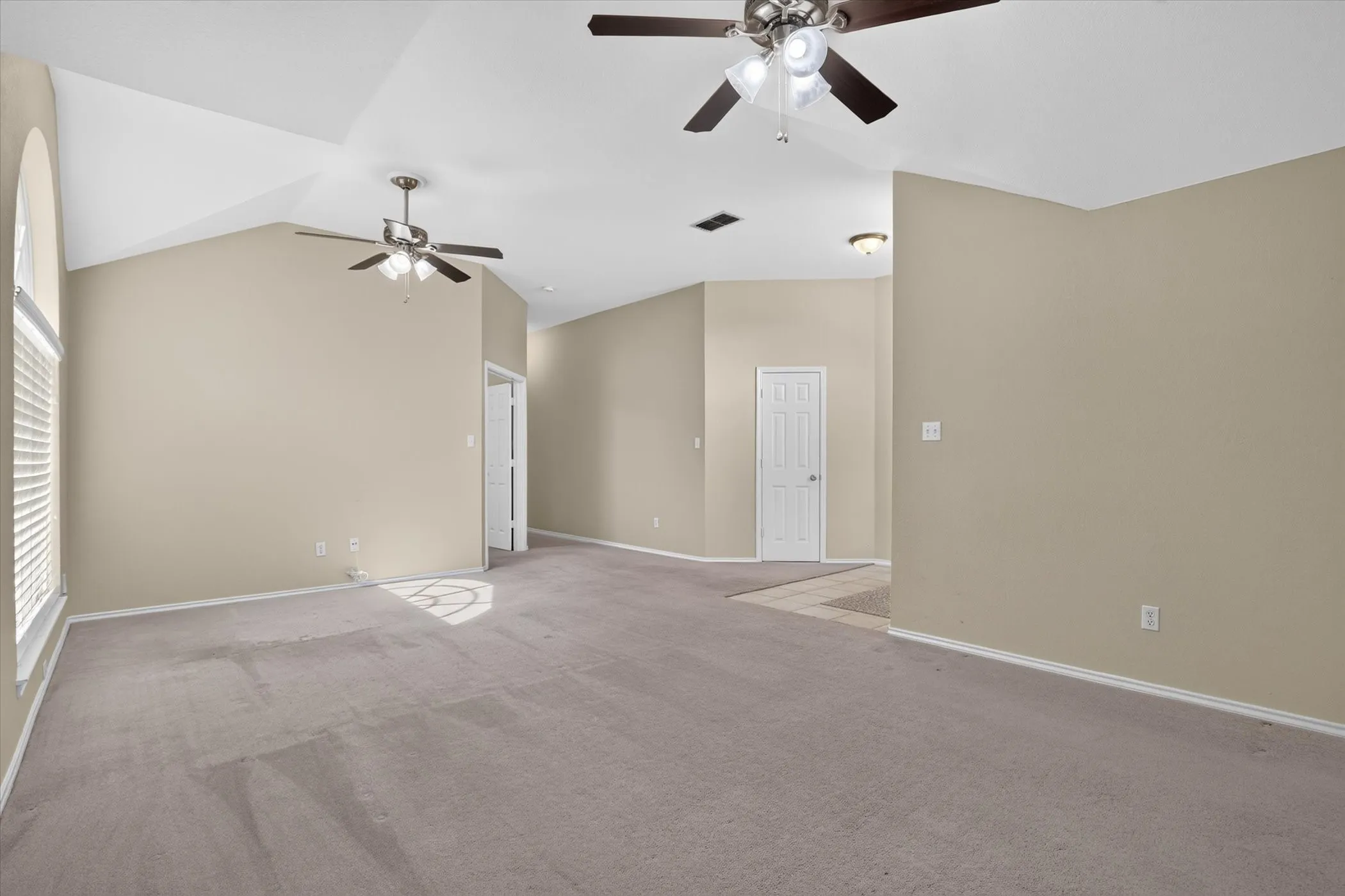 Spacious primary living area with soaring vaulted ceilings, ceiling fans with integrated lighting, and neutral wall finishes