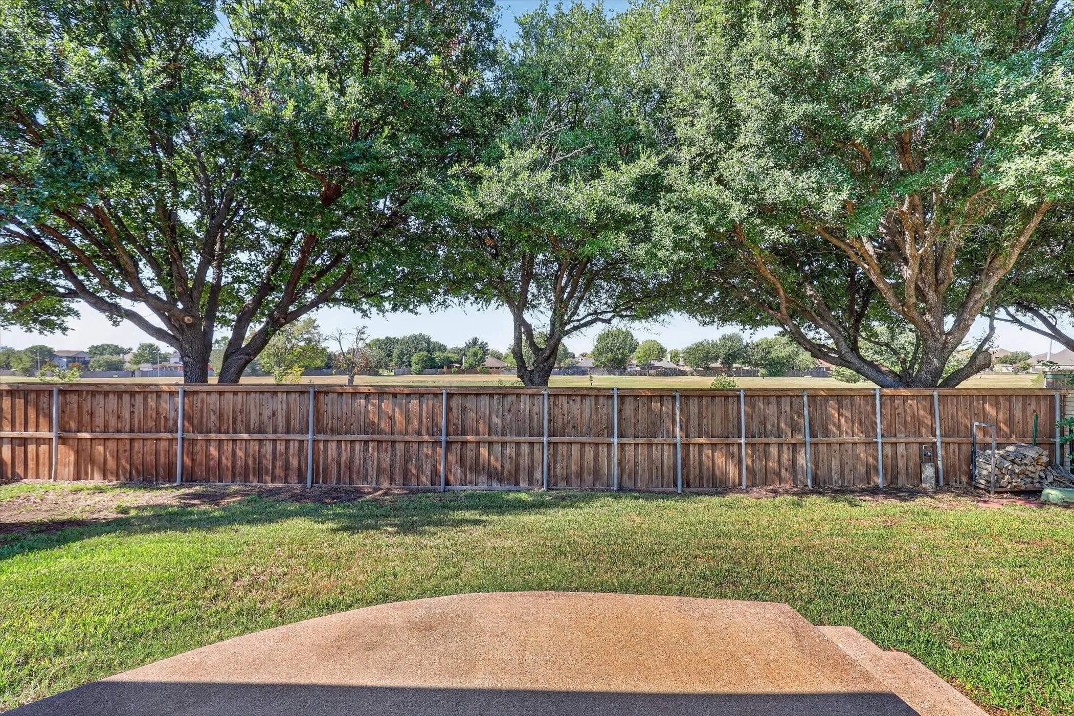 Private backyard with a wood fence, mature trees, and a concrete patio