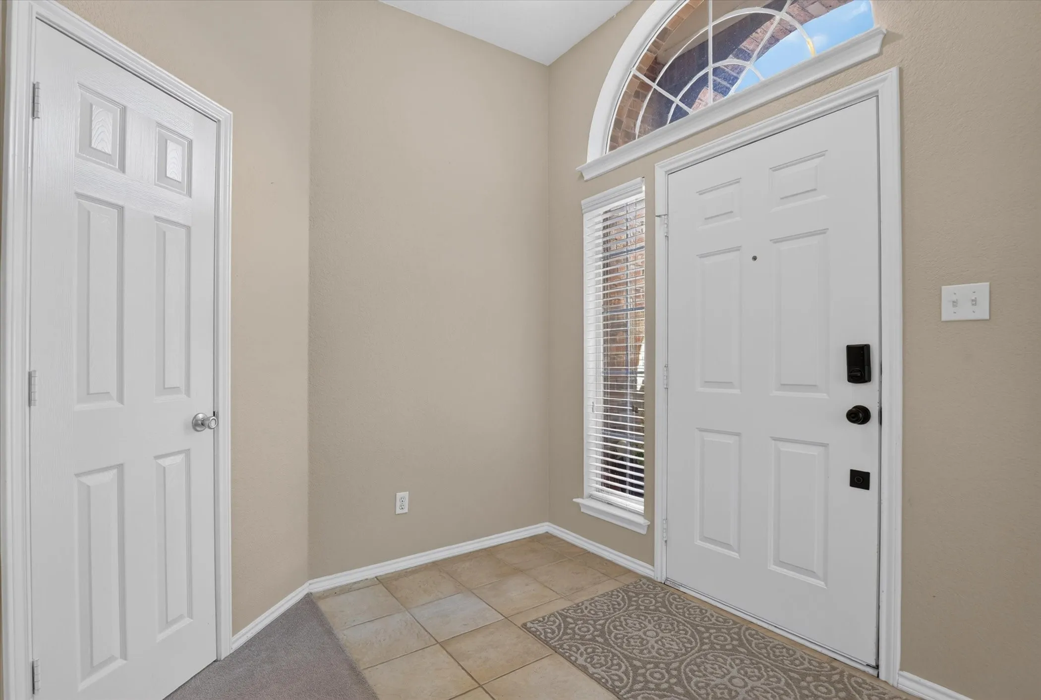 Welcoming foyer showcasing elegant tile flooring, neutral wall finishes, and abundant natural light from a transom window