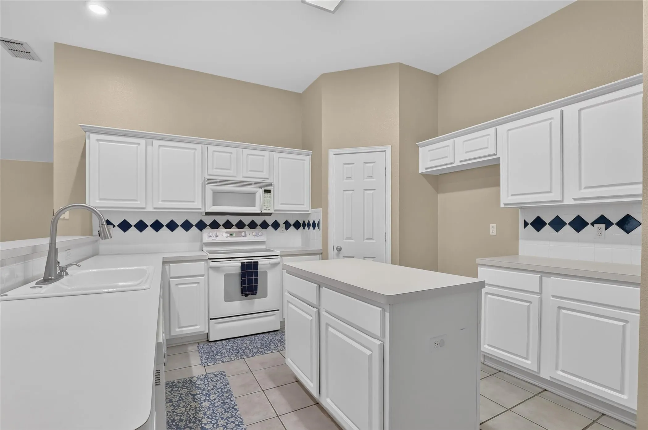 Chef's kitchen featuring white raised-panel cabinetry, stainless steel appliances, tile flooring, and a decorative tile backsplash with navy diamond accents
