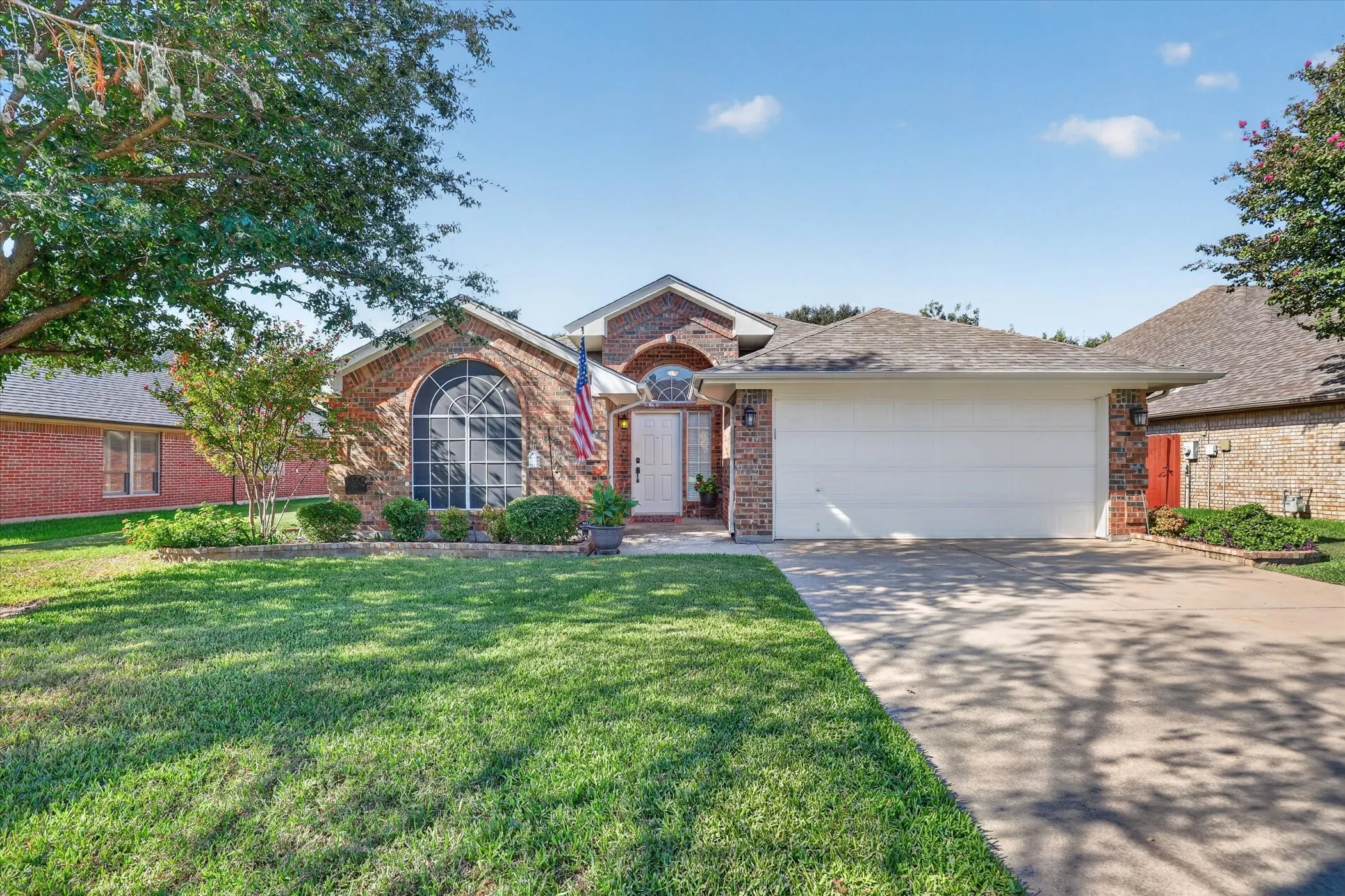 Brick exterior with arched window, landscaped front yard, attached two-car garage, and concrete driveway