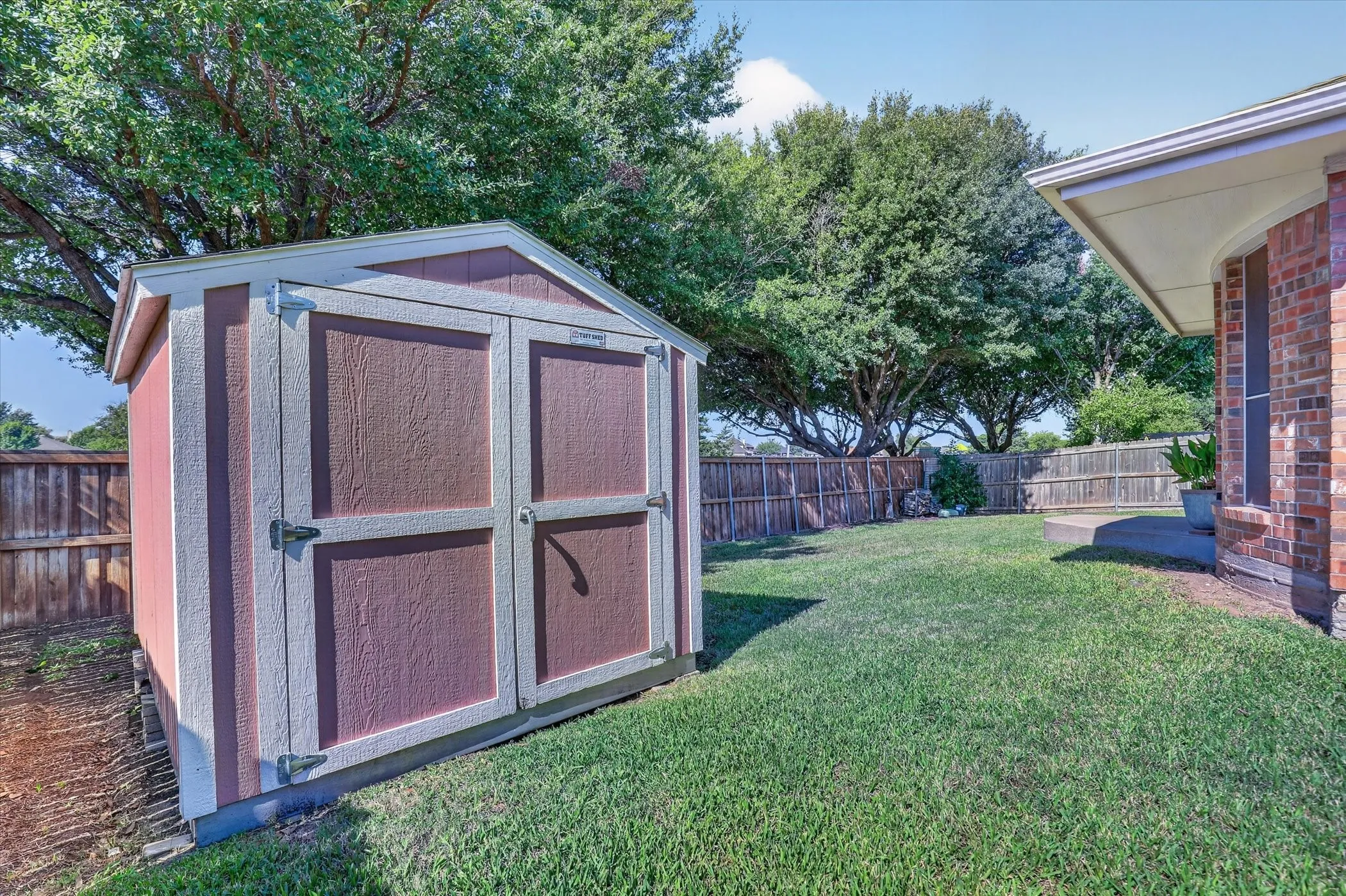 Spacious backyard retreat featuring a custom storage shed with double doors and durable wood-finish paneling, mature shade trees, and manicured lawn